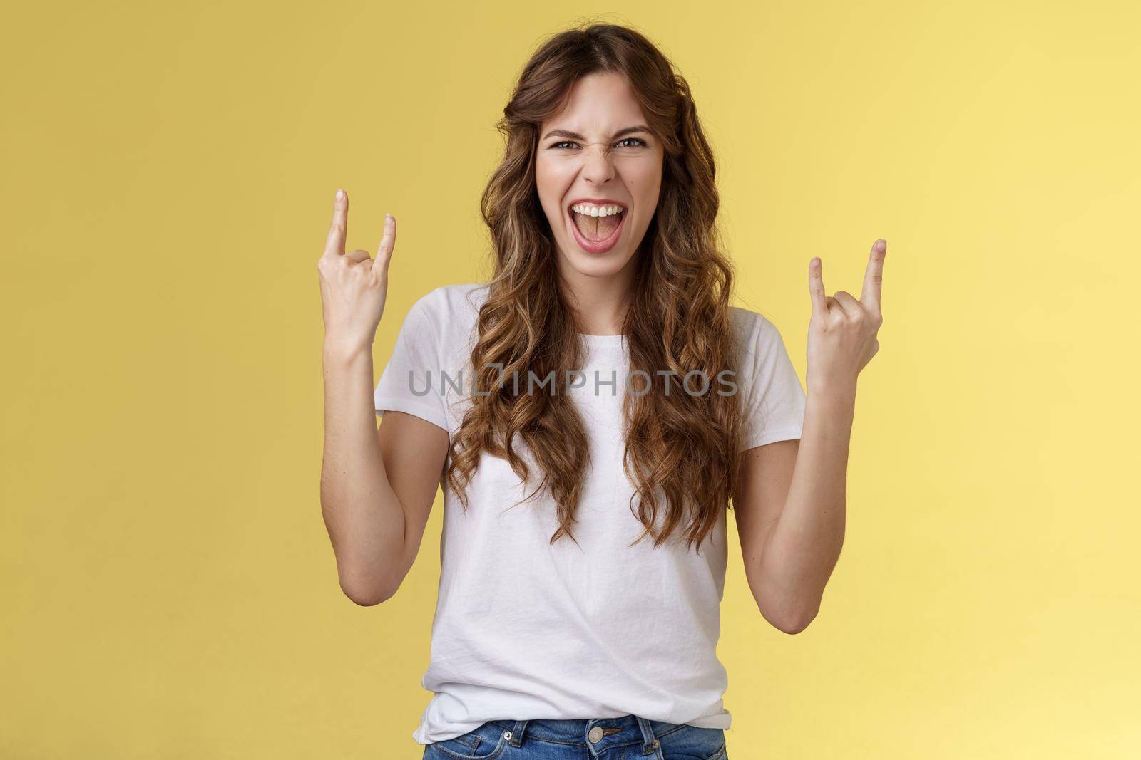 Going wild. Daring amused good-looking european curly-haired girl acting thrilled excited having fun enjoy awesome concert show yeah rock-n-roll heavy metal gesture grimacing satisfied by Benzoix