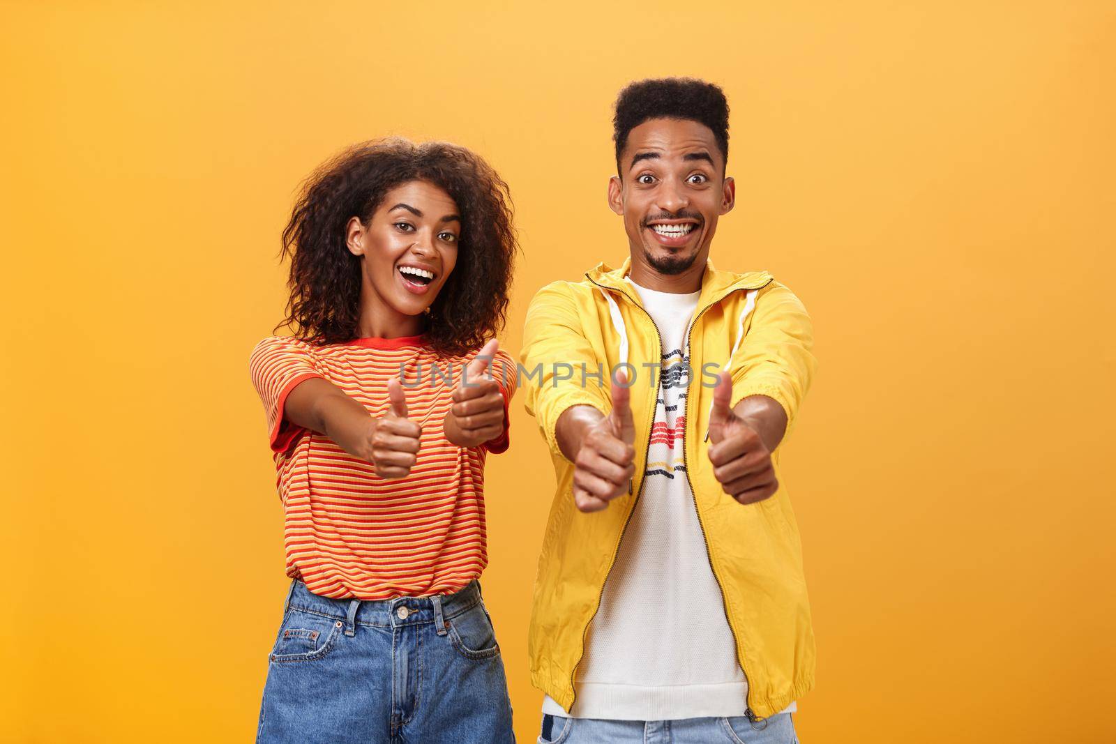 Two friends like perfect and awesome plan. Portrait of joyful friendly-looking optimistic african american female and male showing thumbs up in approval and agreement gesture smiling broadly. Copy space