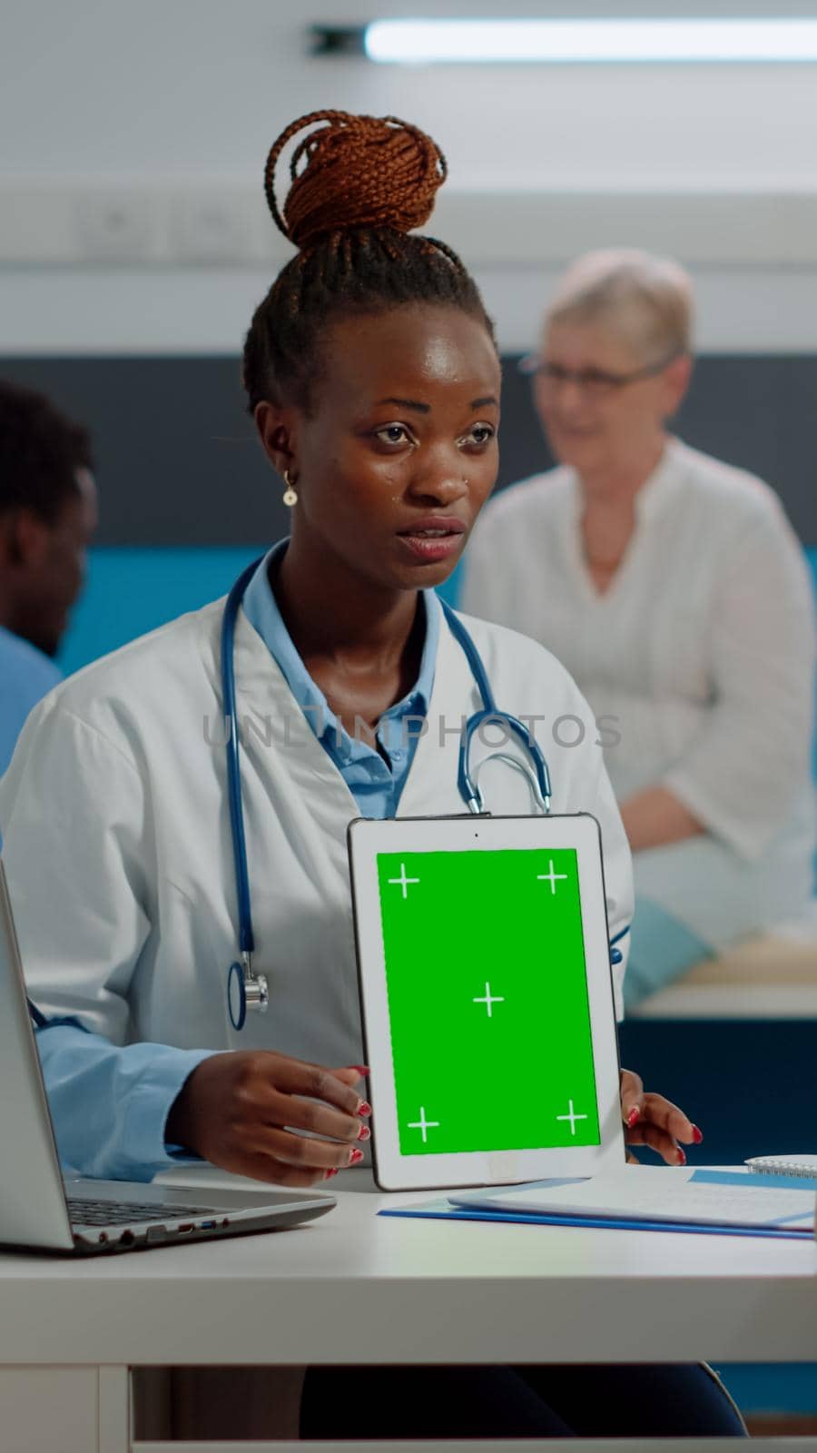 Medic showing green screen on tablet to senior man sitting at desk in healthcare office at hospital. Doctor vertically holding isolated template with mockup background and chroma key.