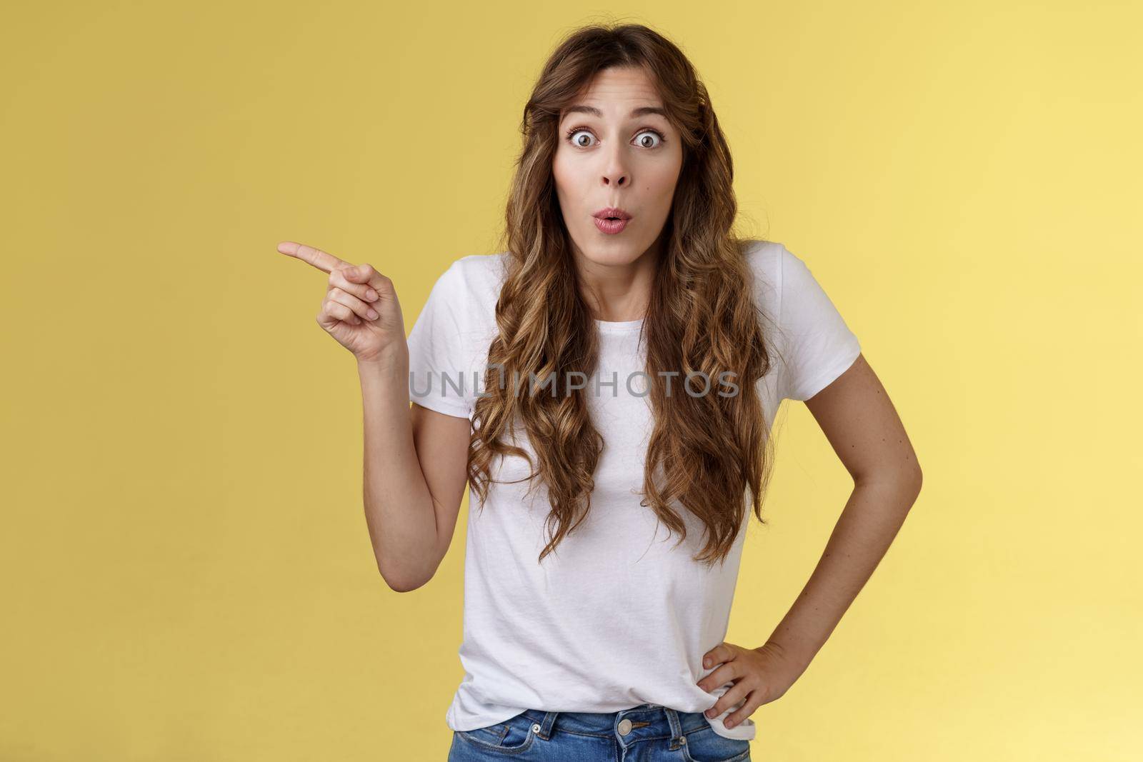 Wow incredible lets click. Impressed surprised pretty european woman long curly hairstyle folding lips intrigued stare astonished wondered awesome cool promo offer pointing left yellow background by Benzoix