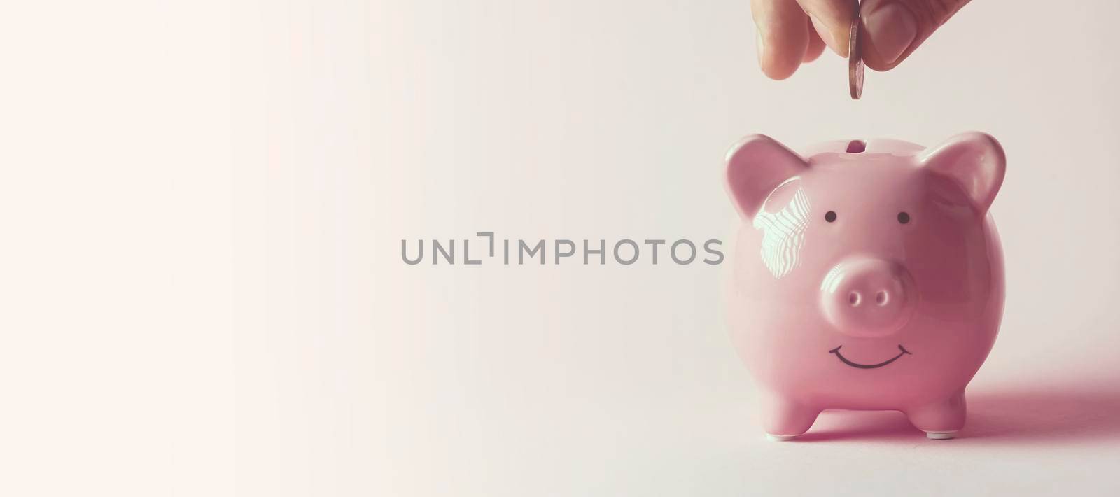 The hand holds a coin and puts it in a piggy bank to preserve wealth, savings and financial success.
