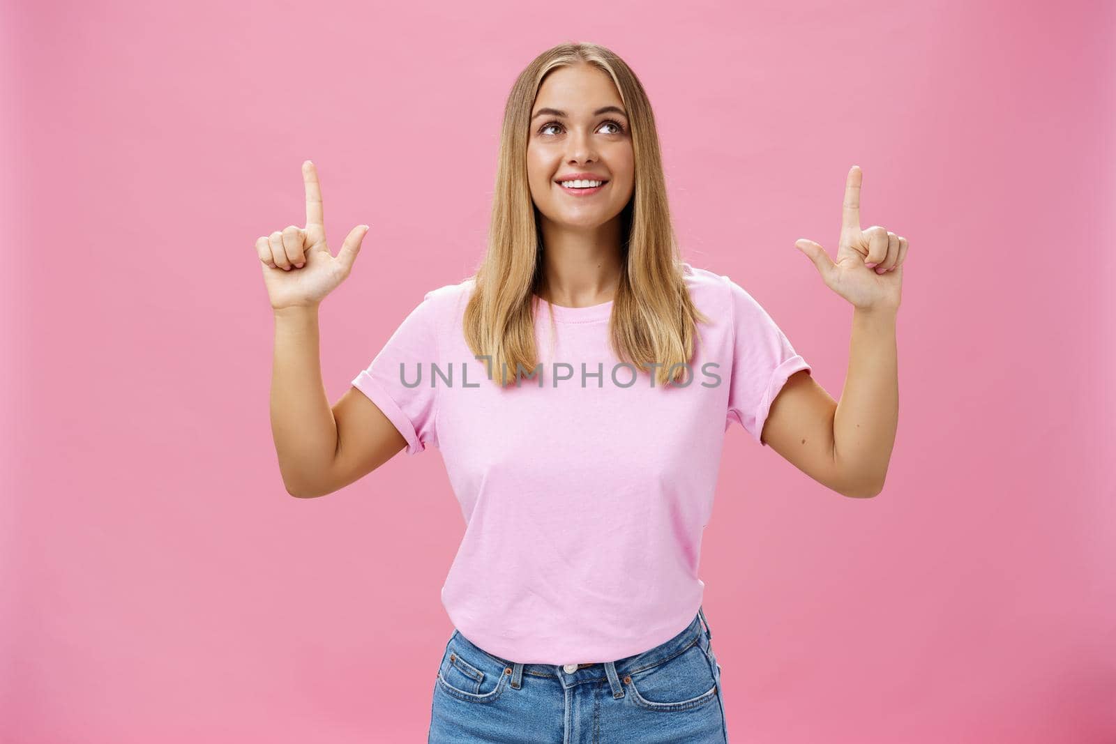 Girl daydreaming pointing and looking with upbeat and admiring expression up smiling cheerfully enjoying nice sunny weather walking in casual t-shirt and jeans posing against pink background by Benzoix