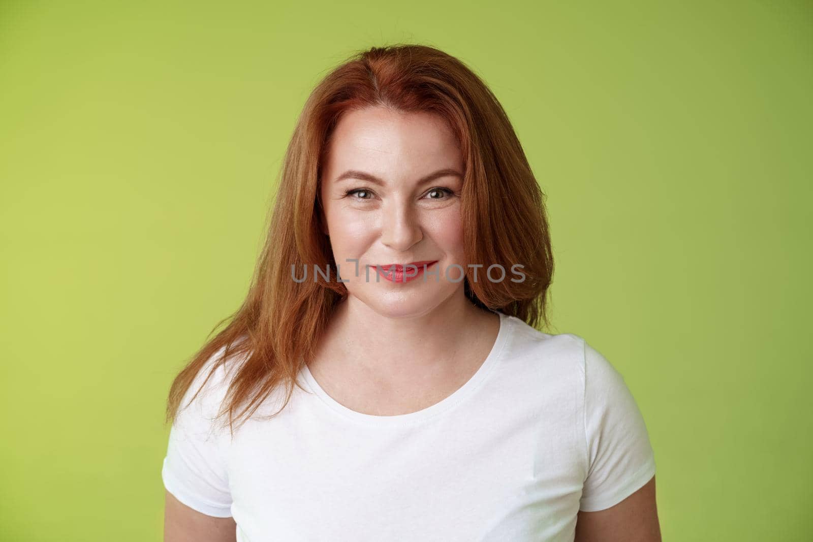 Enthusiastic smiling redhead middle-aged woman grinning joyfully. alluring motivated gaze camera determined reach goal happy watching grandson playing yard pleased have perfect family green background.