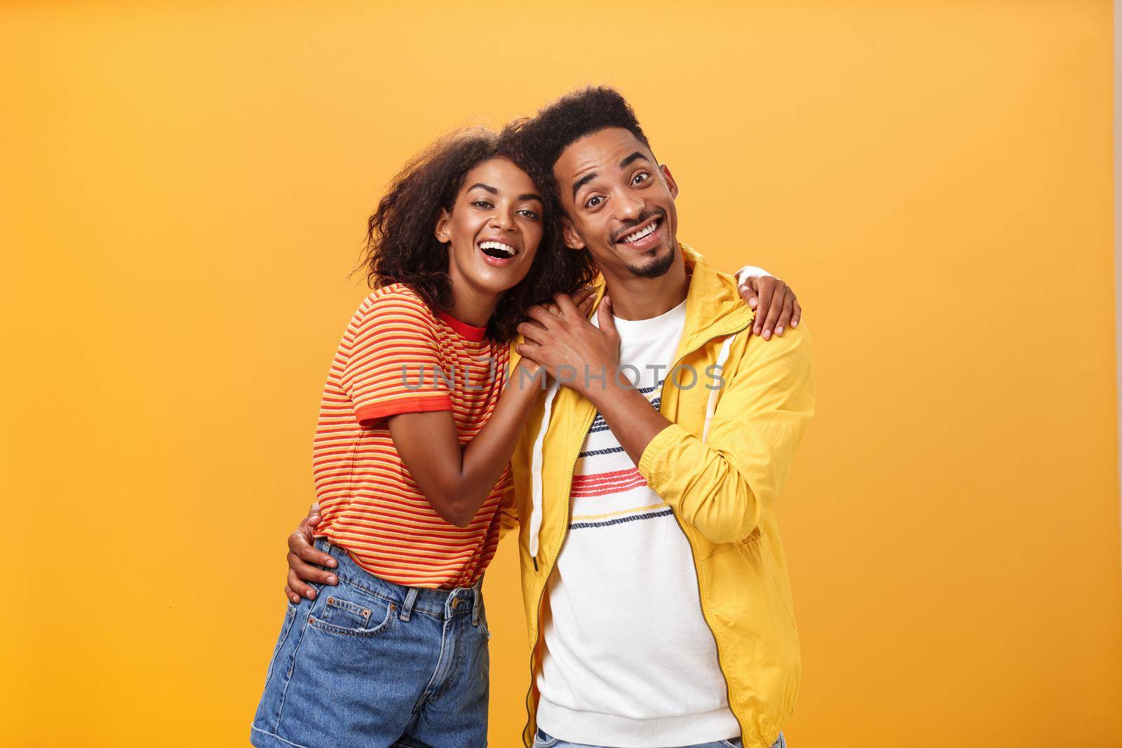 Friends always cover each other. Stylish and carefree loving african american girlfriend hugging boyfriend and smiling broadly touching guy palm hanging around and spending time great together.