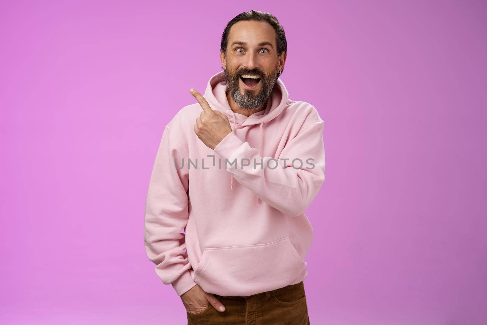 Speechless excited impressed handsome bearded man grey hair widen eyes surprised astonished wow drop jaw gasping thrilled pointing upper left corner see famous star, purple background.