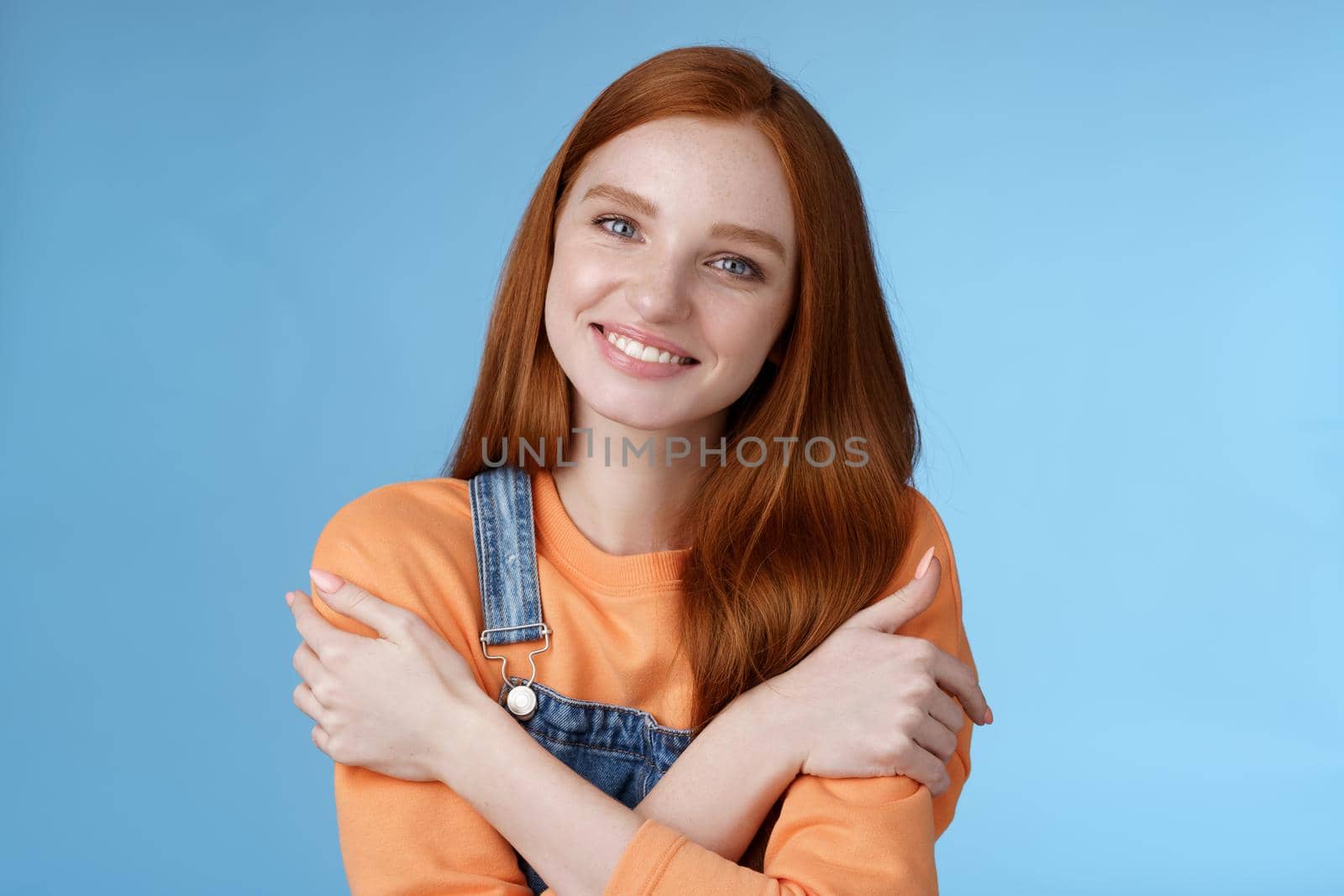 Lifestyle. Tender silly redhead girl standing blue background smiling joyfully hugging arms crossed body feel chilly grinning delighted talking boyfriend romantic date asking lend jacket cold summer evening.