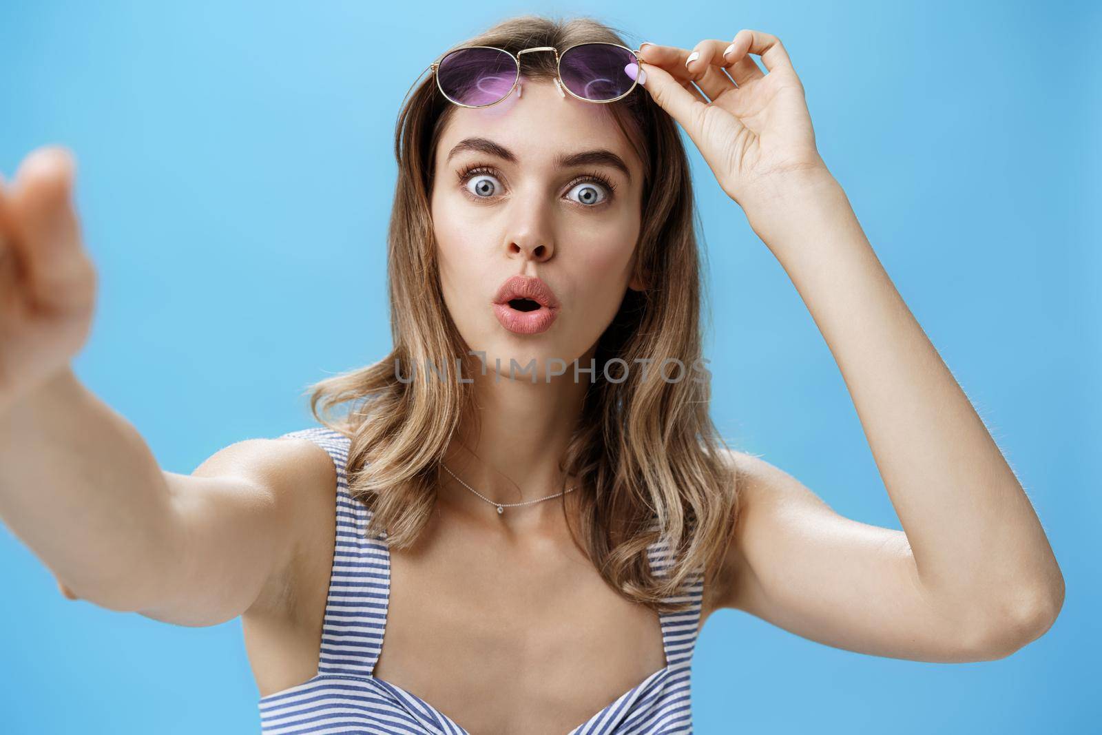 Woman taking off glasses while looking at herself in frontal camera of smartphone holding cellphone taking selfie being stunned and amazed with super cool thing folding lips from interest. Lifestyle.