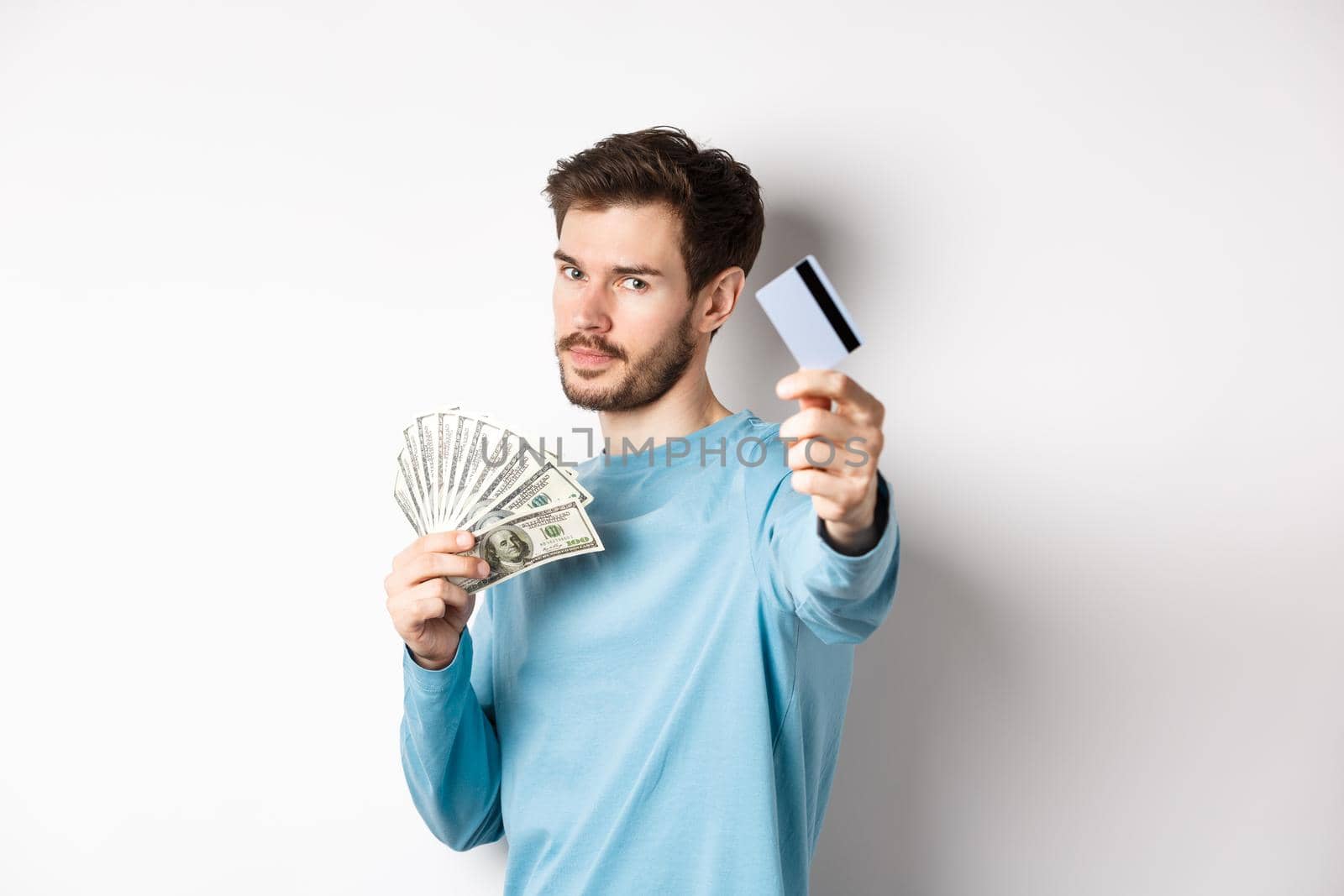 Serious-looking guy stretch out hand with plastic credit card, prefer contactless payment instead of cash, standing on white background.