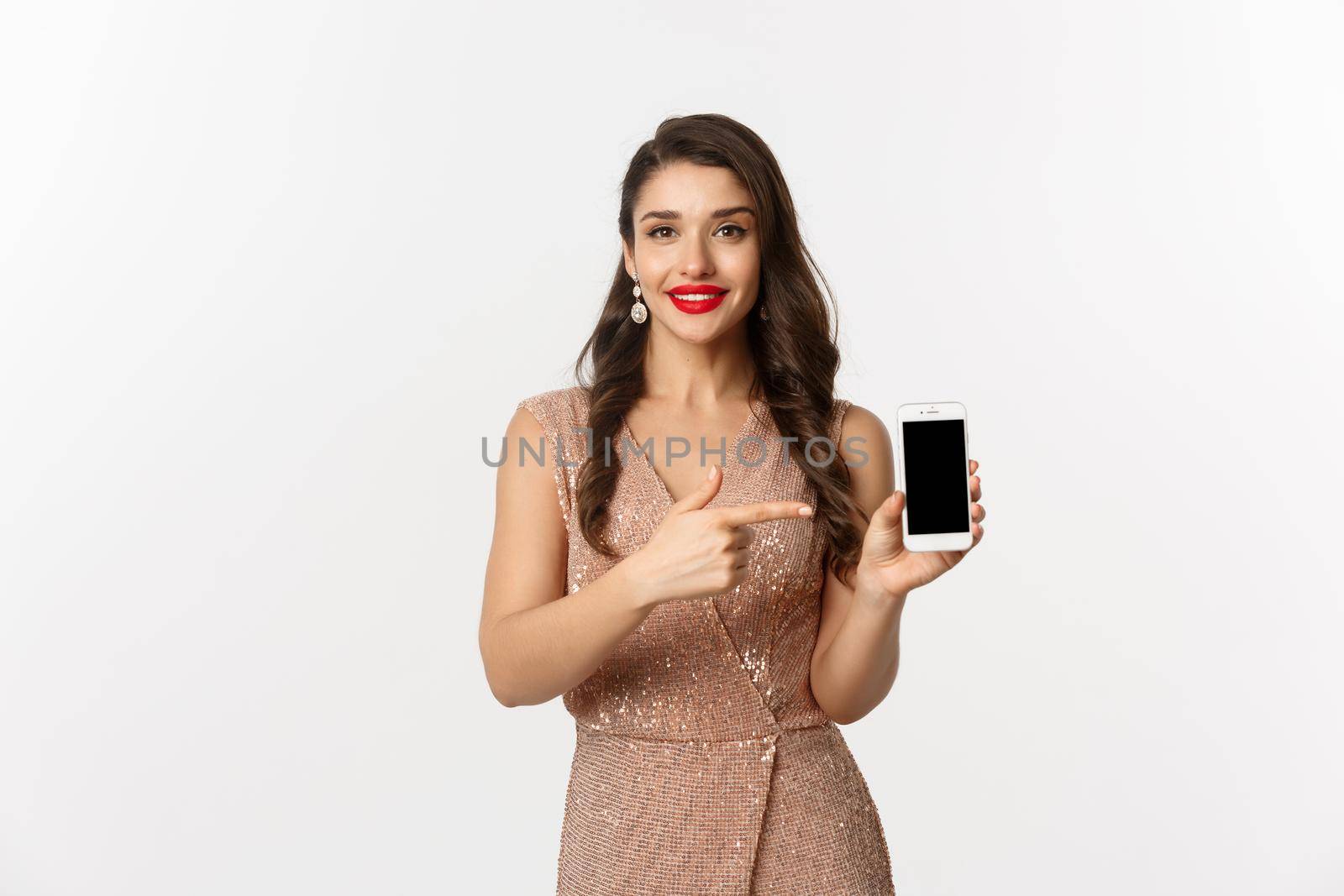 Online shopping. Good-looking woman with red lipstick, luxury dress, pointing finger at mobile screen, showing internet store or app, white background.