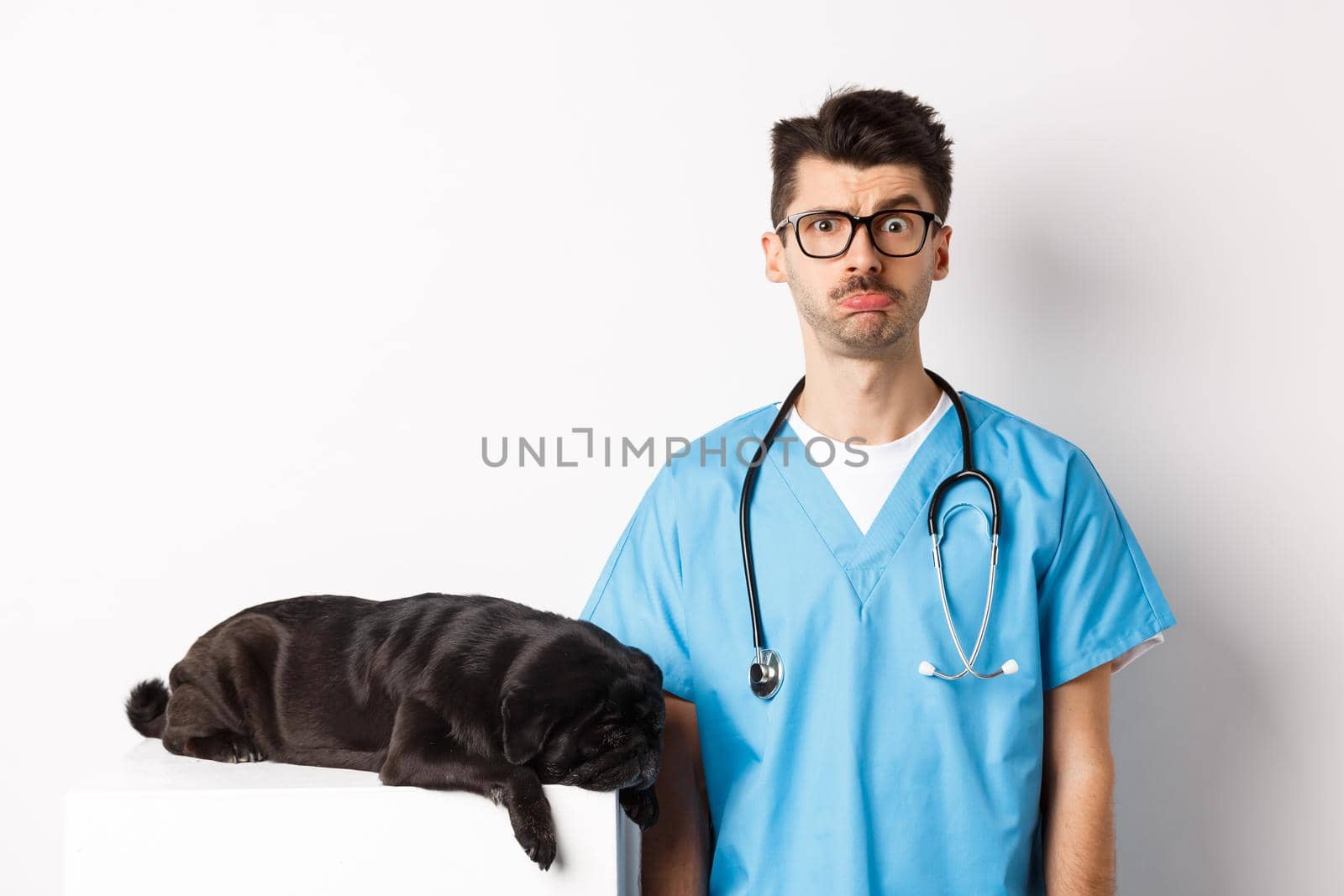 Tired black dog pug lying near handsome male doctor at veterinary clinic, veterinarian staring confused at camera, standing over white background by Benzoix