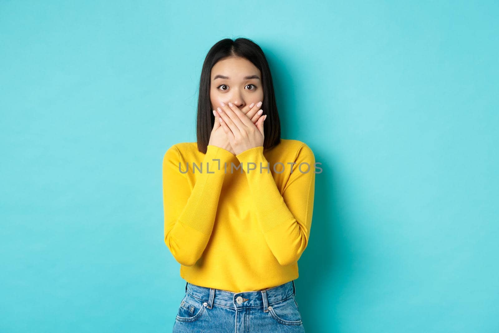 Image of shocked asian girl cover mouth and staring at camera, wearing yellow sweater against blue background by Benzoix