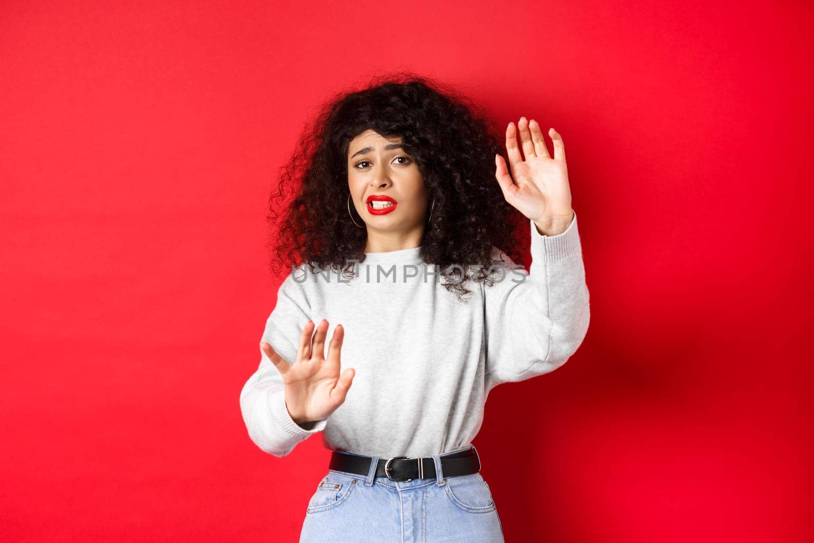 Disgusted young woman begging to stop, raising hands defensive, say no, standing on red background by Benzoix