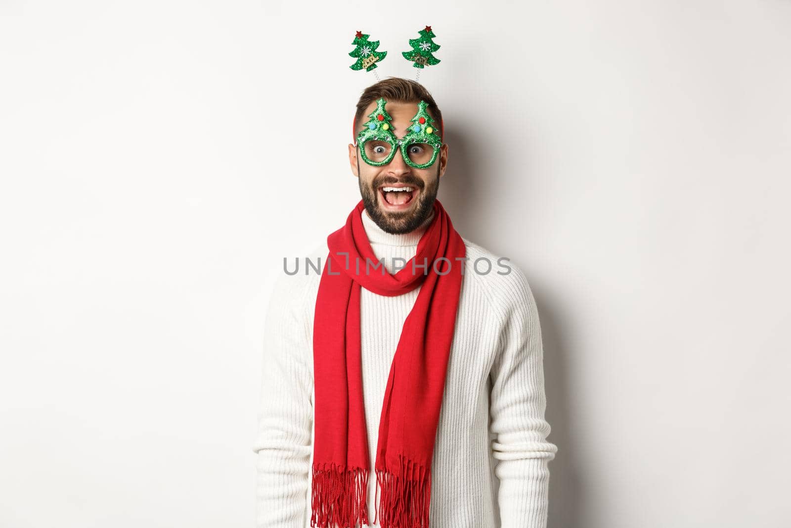 Christmas, New Year and celebration concept. Handsome bearded man looking surprised, wearing party glasses and accessory, white background by Benzoix