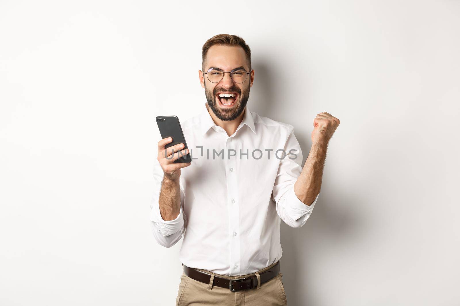 Successful businessman looking happy, fist pump and rejoice in winning online lottery, standing over white background.