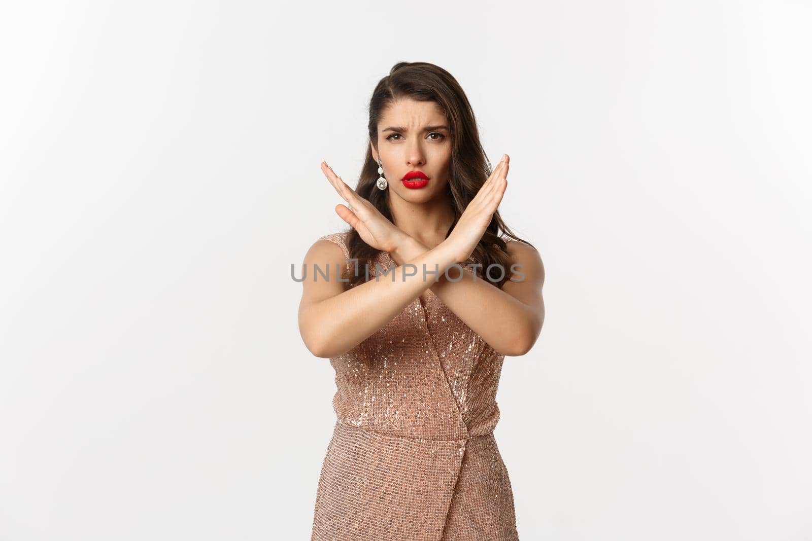 Displeased young woman in luxurious dress and red lipstick saying no, showing stop sign, cross gesture to refuse or prohibit, standing over white background by Benzoix