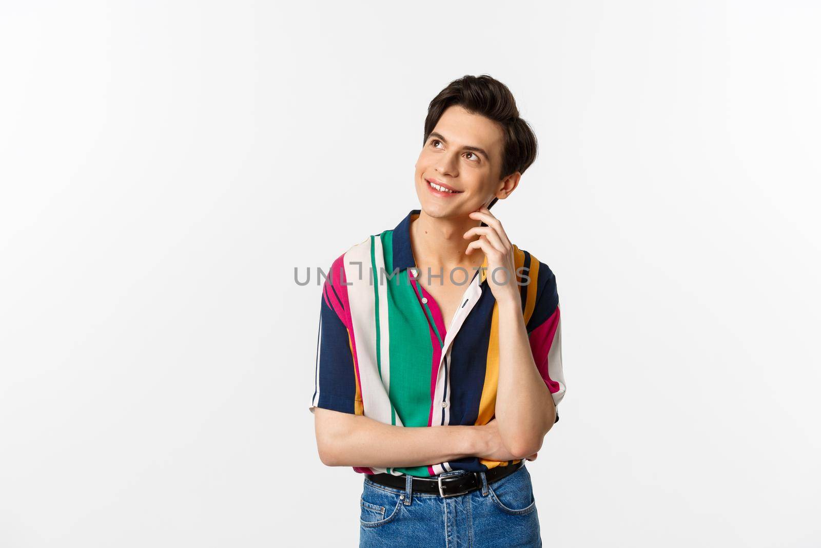 Thoughtful smiling gay man looking at upper left corner, imaging something, standing over white background.