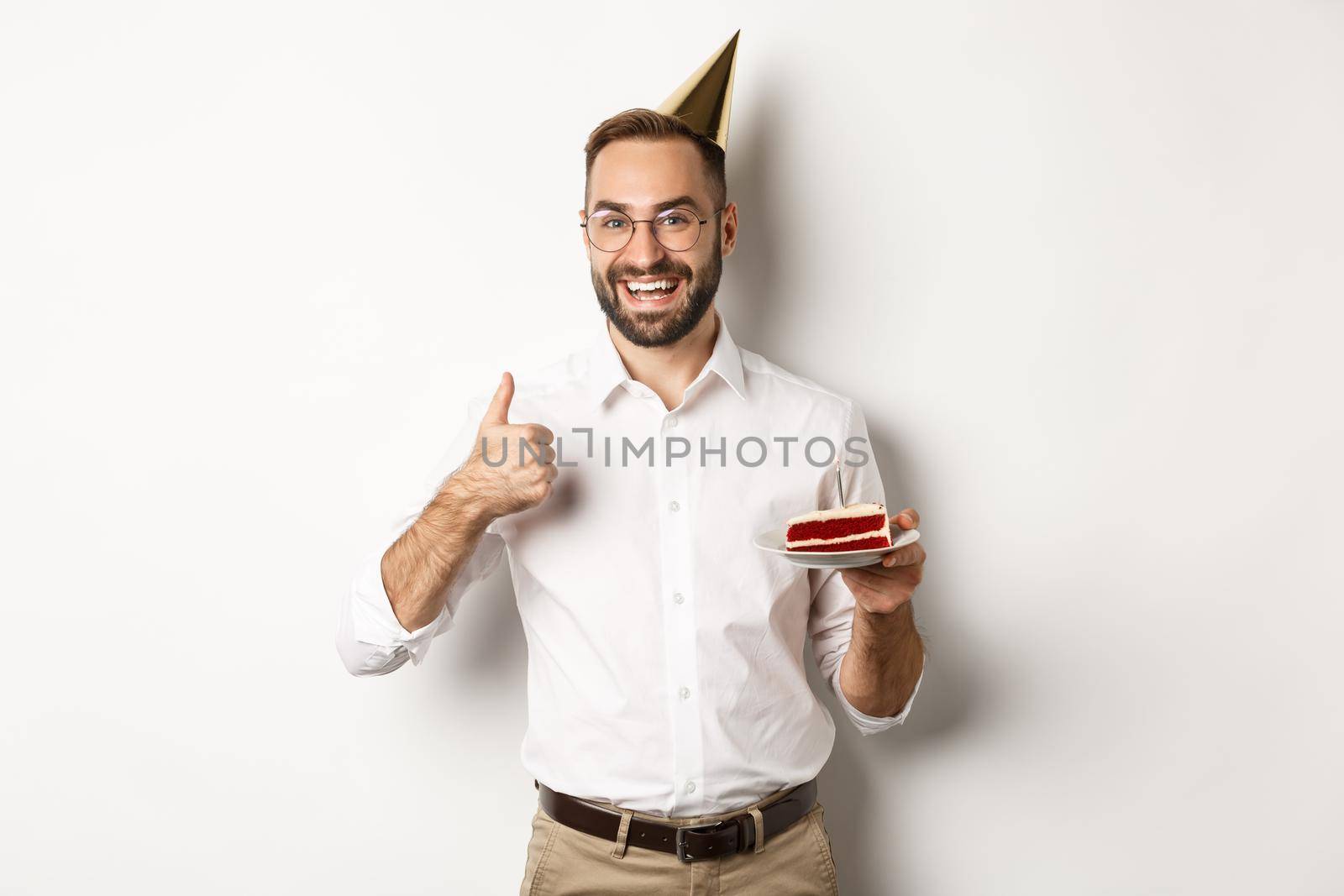 Holidays and celebration. Satisfied man enjoying b-day party, holding birthday cake and showing thumb up in approval, recommending something, white background by Benzoix
