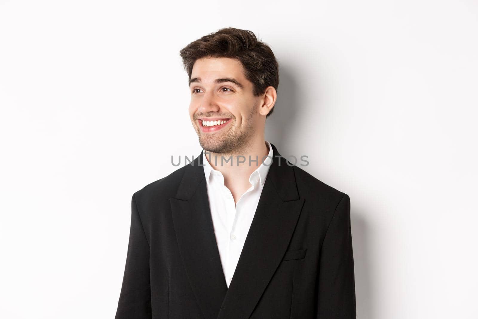 Close-up of handsome male entrepreneur in suit, looking left and smiling, standing against white background.