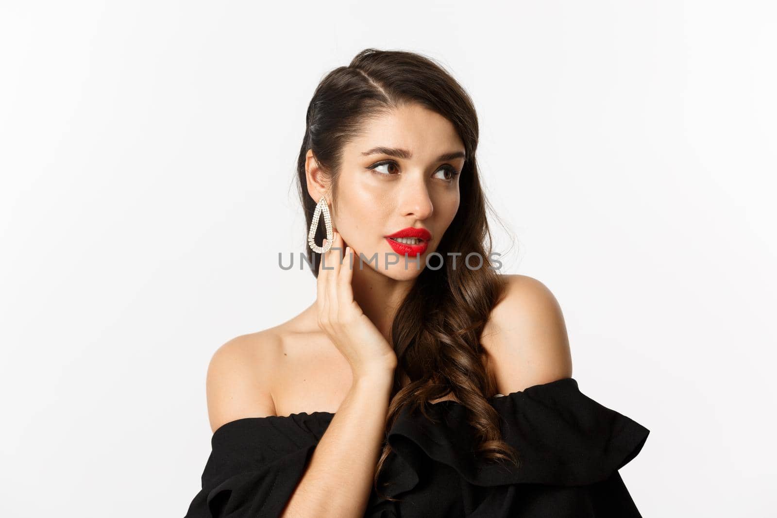 Fashion and beauty concept. Close-up of elegant woman in black dress, showing earrings and looking sensual, red lipstick and makeup on, white background by Benzoix