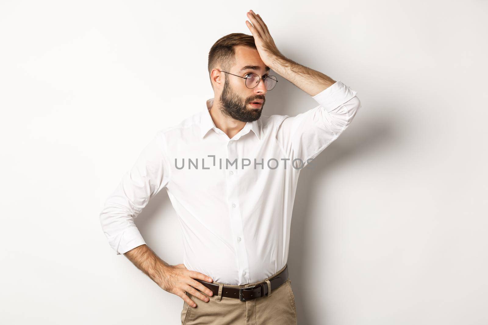 Annoyed man manager roll his eyes and slap forehead, facepalm from something tiresome, standing over white background.