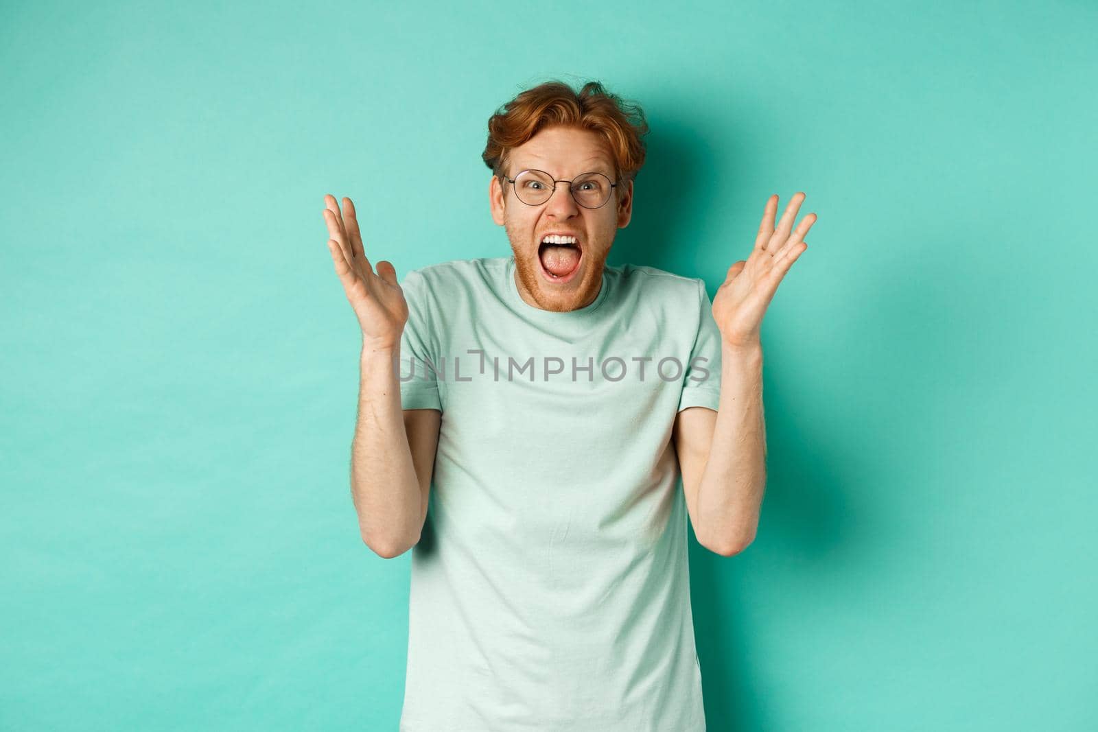 Portrait of distressed and angry redhead guy losing temper, shouting and shaking hands outraged, staring with furious face at camera, standing over mint background by Benzoix