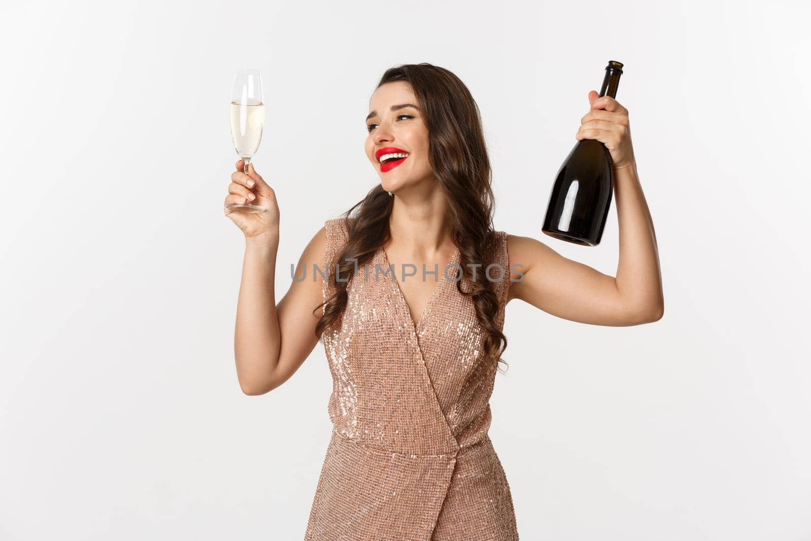 Winter holidays celebration concept. Excited beautiful woman in dress raising glass of champagne for toast, enjoying Christmas party, standig over white background.