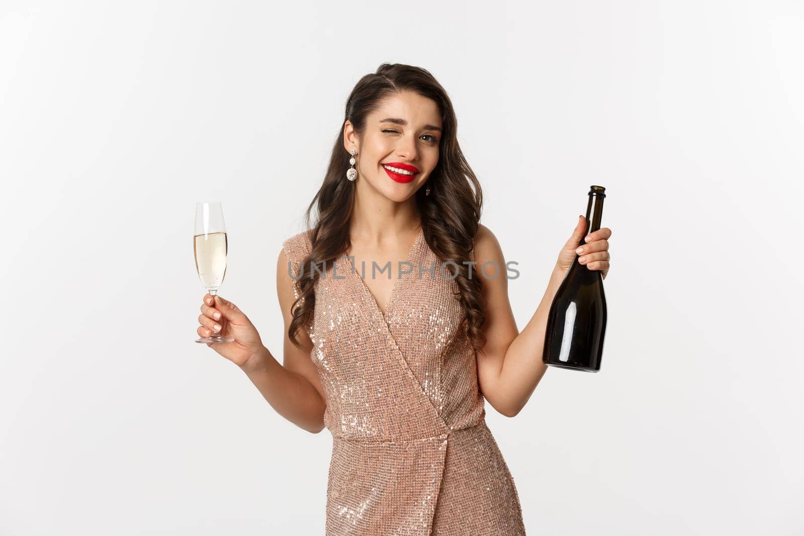 Winter holidays celebration concept. Beautiful woman enjoying Christmas and New Year party, drinking champagne and winking at camera, standing in elegant dress by Benzoix
