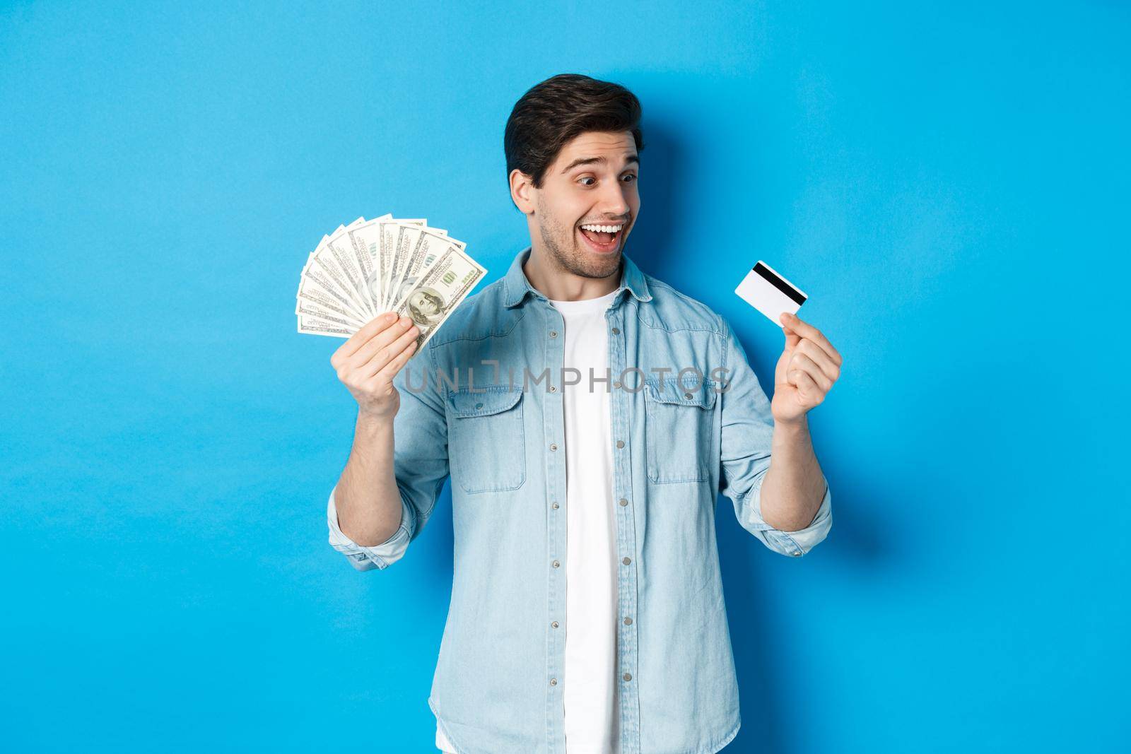Surprised and happy man looking at credit card and showing money, concept of bank loan, finance and income. Copy space