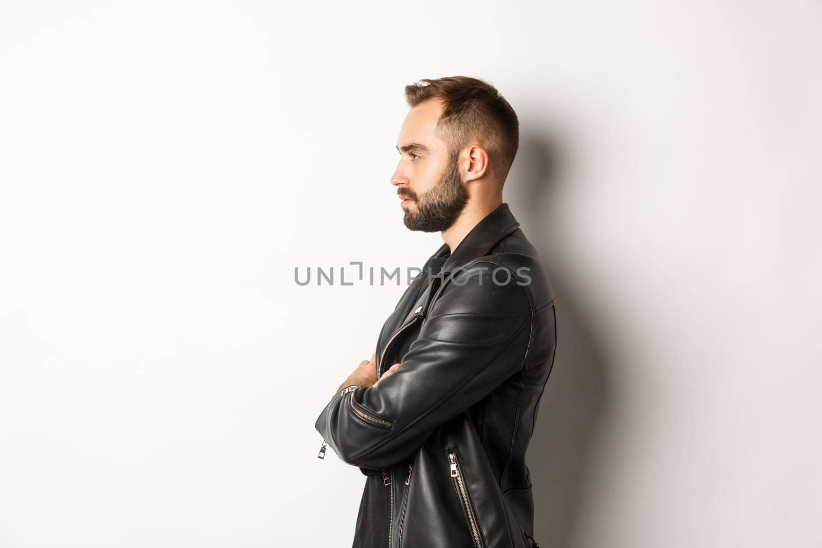 Profile of handsome serious man in leather jacket, looking left, holding hands on chest confident, white background.