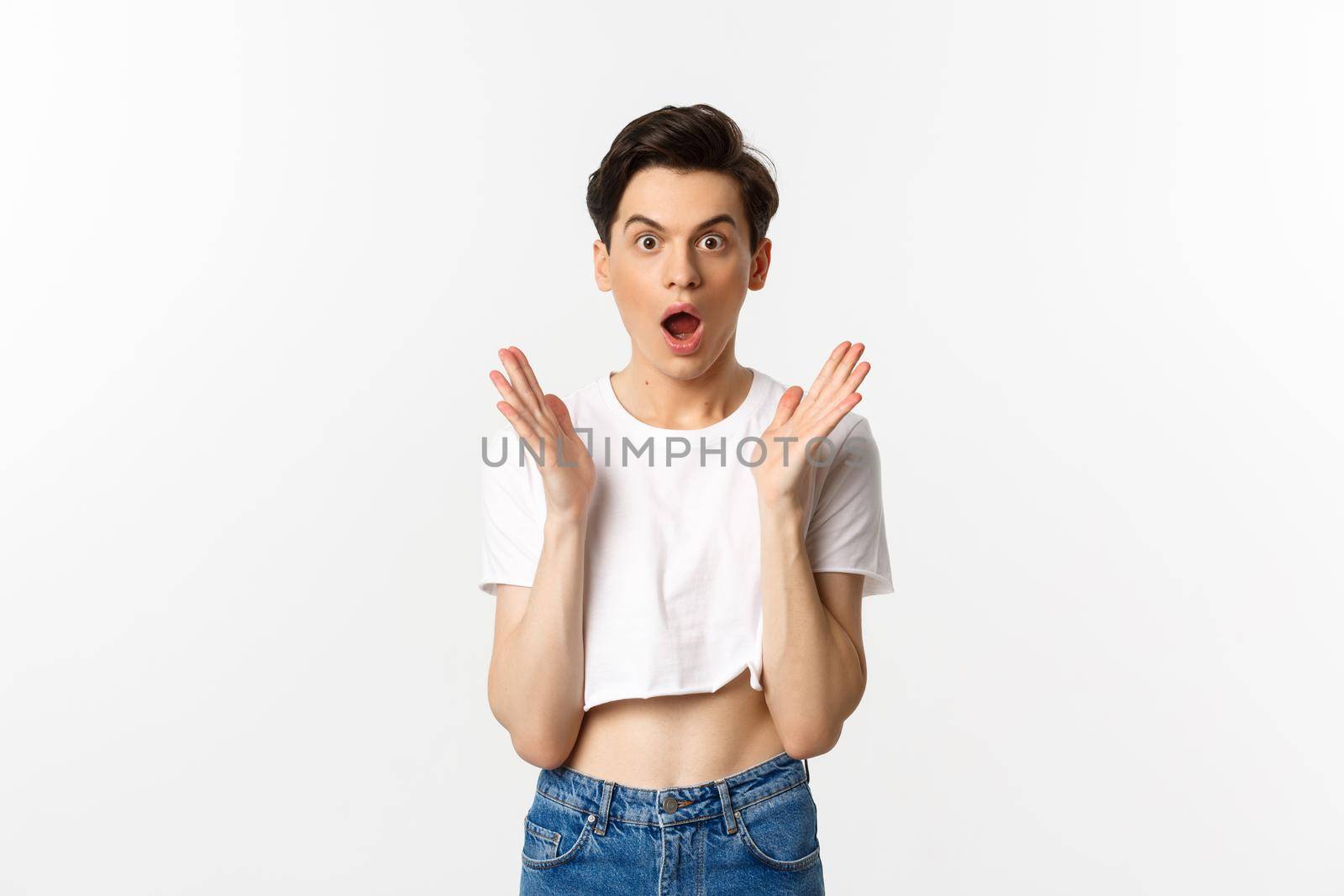 Lgbtq and pride concept. Image of surprised queer guy clap hands and looking in awe at camera, standing in crop top against white background.
