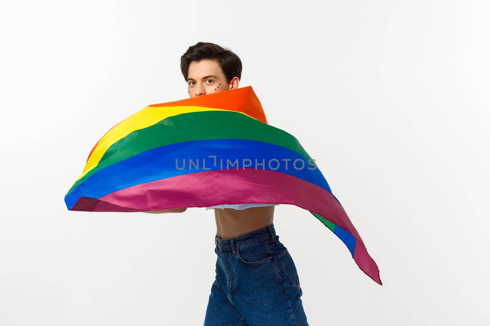 Human rights and lgbtq community concept. Young queer person with glitter on face, waving lgbtq flag with pride, standing over white background.