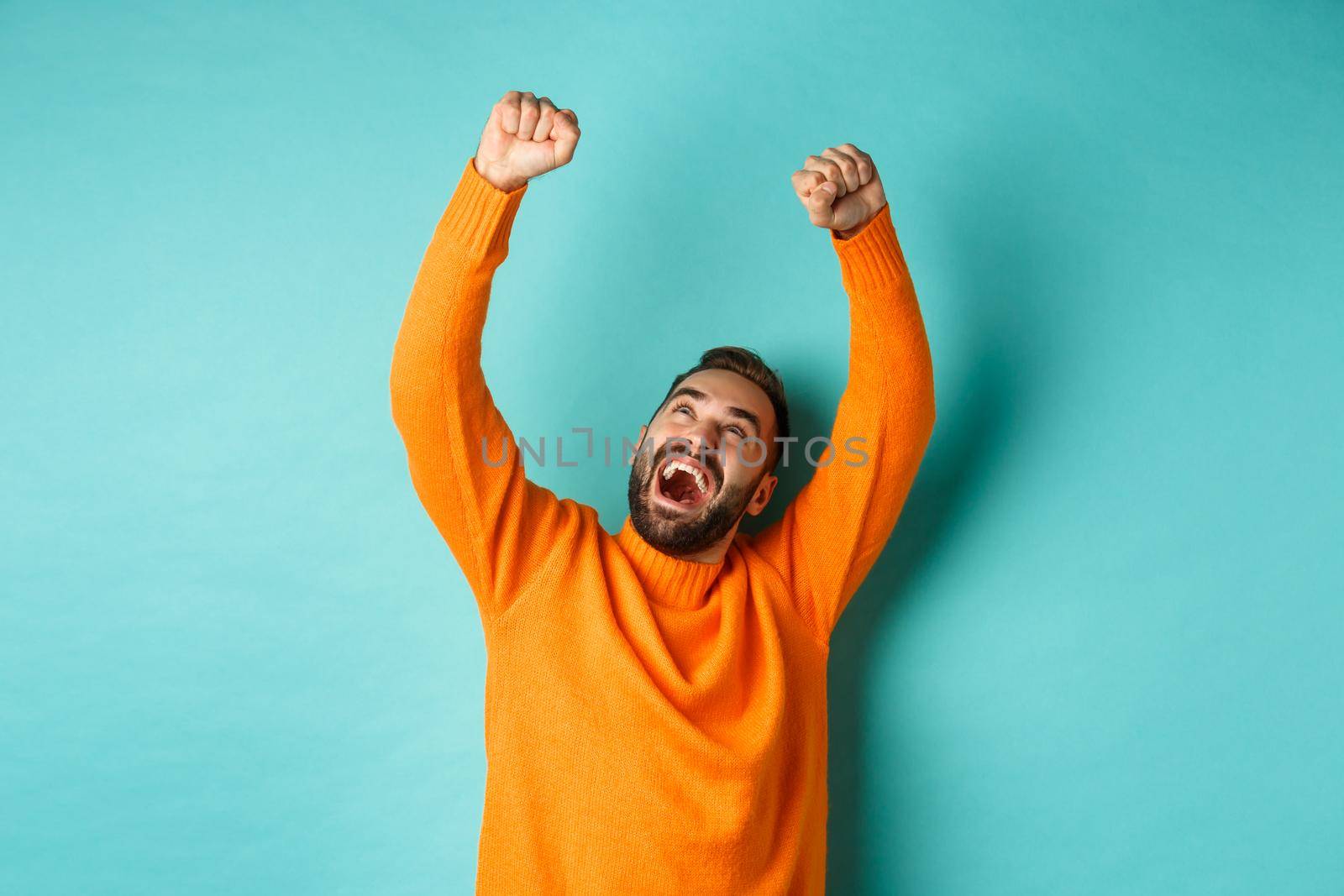 Happy man triumphing and feeling rejoice of winning, celebrating victory, standing over light blue background. Copy space