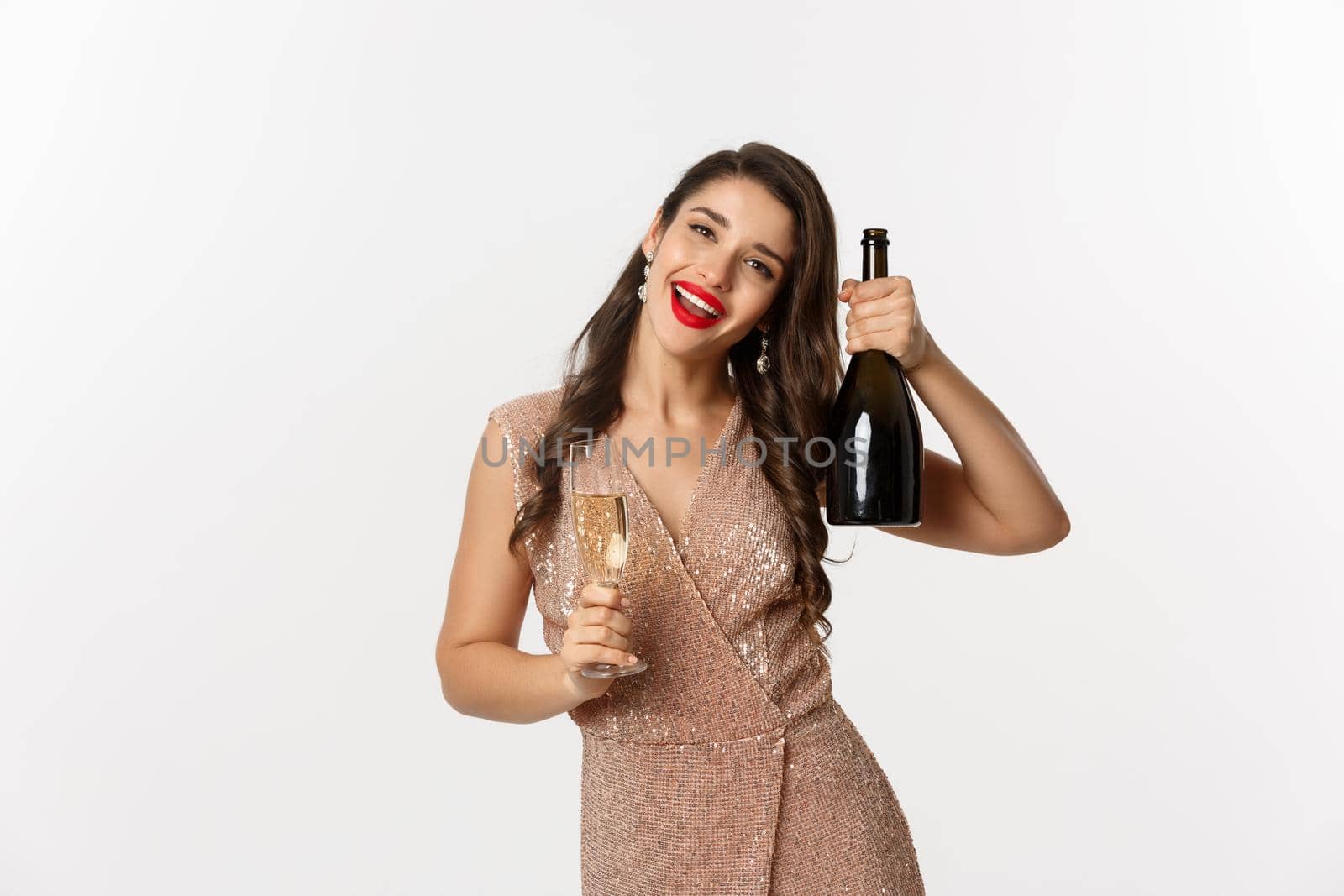 Winter holidays celebration concept. Happy woman on Christmas party saying cheers, raising bottle of champagne and smiling, standing in elegant dress, white background.