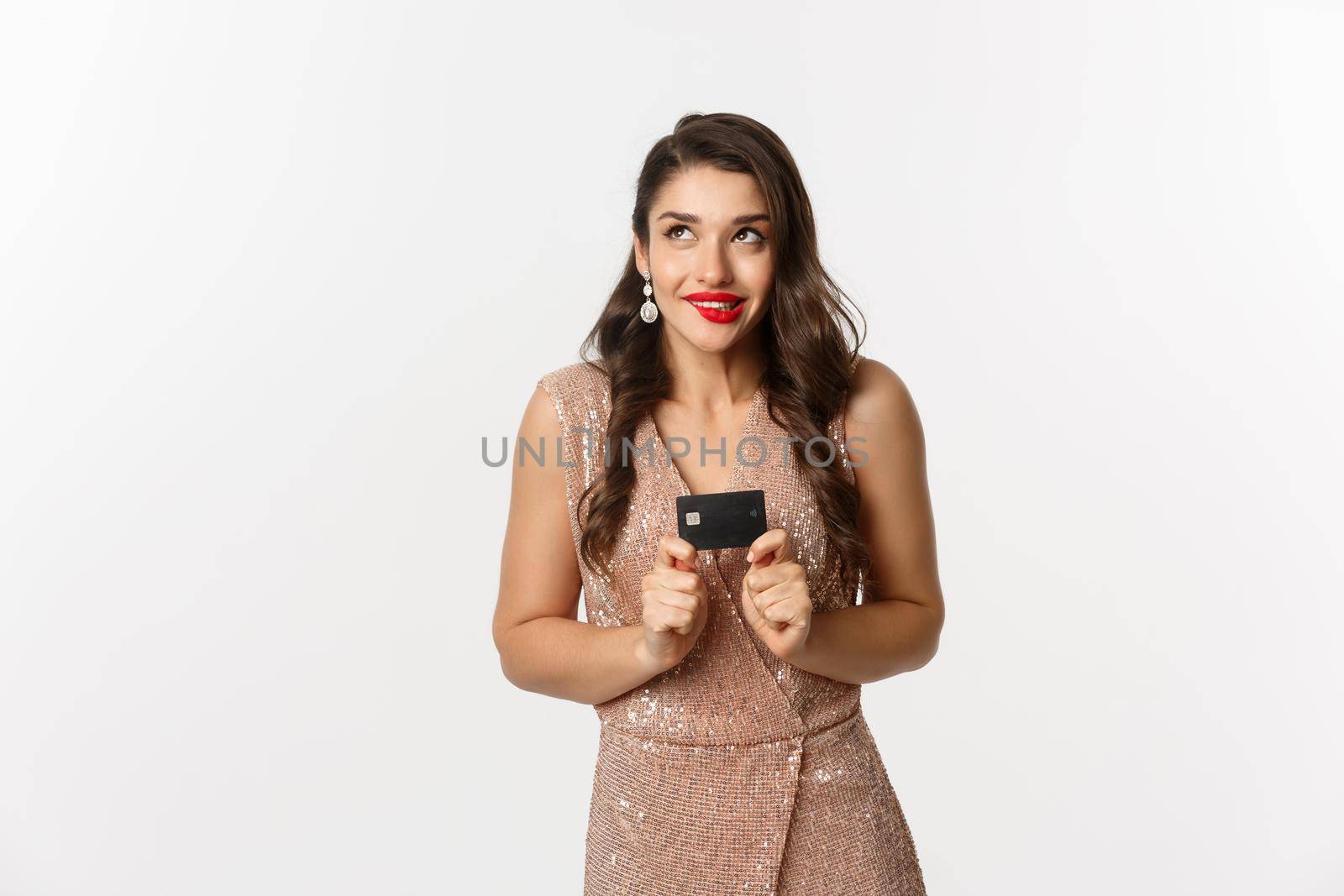 Holidays. christmas party and shopping concept. Beautiful female model in luxury dress thinking and holding credit card, standing over white background.