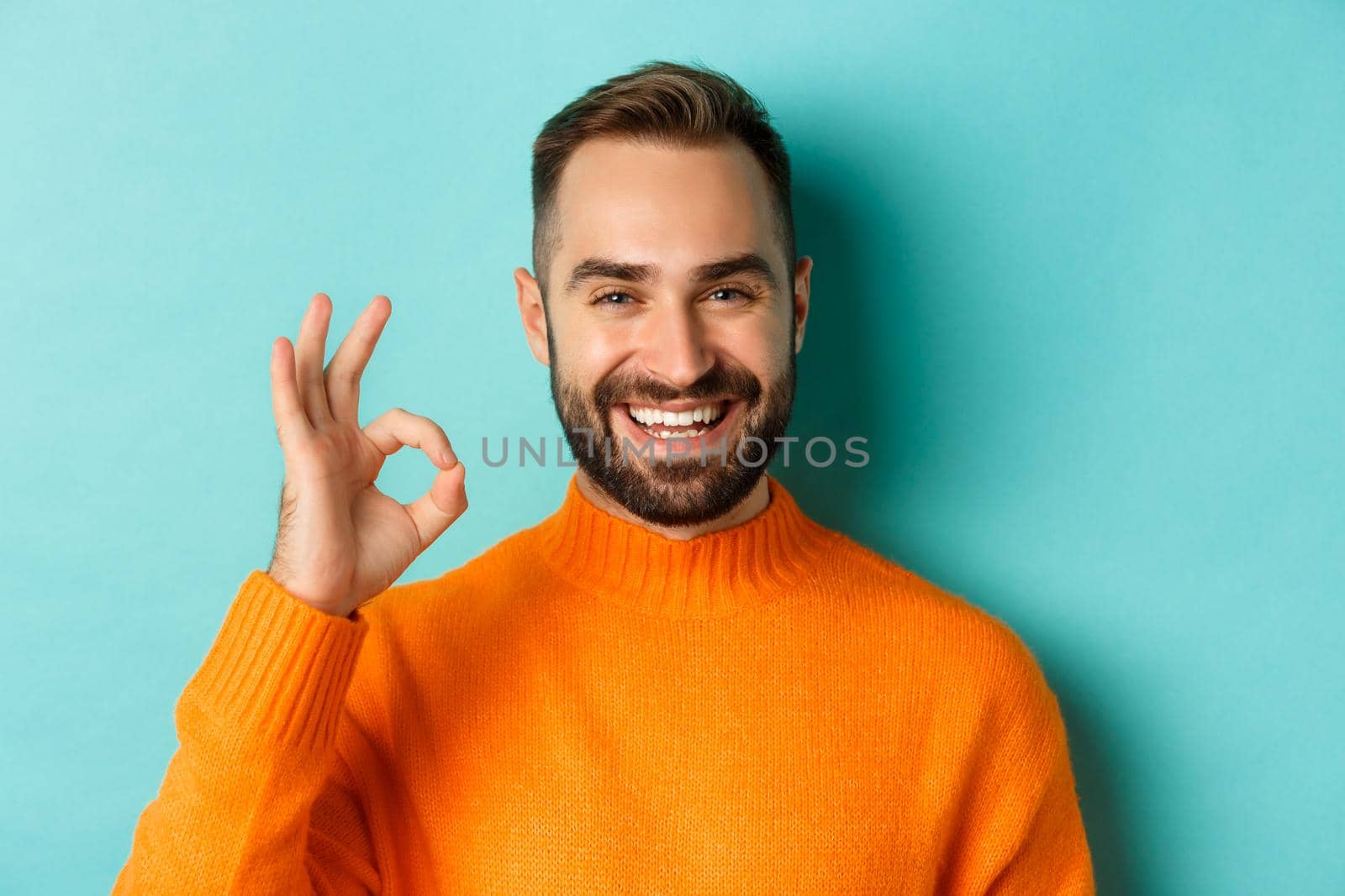 Close-up of assertive young man assuring everything ok, showing okay sign and smiling, yes or positive answer, standing over light blue background by Benzoix