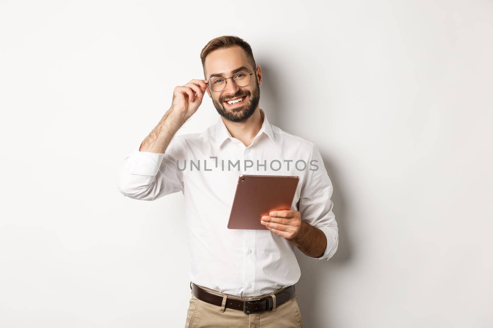 Confident business man working on digital tablet, smiling happy, standing over white background.