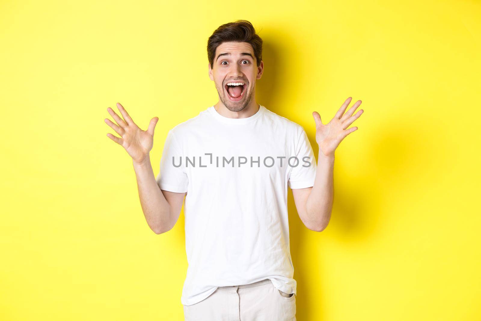 Portrait of excited and surprised man reacting to big promo offer, shouting for joy and triumphing, standing over yellow background.