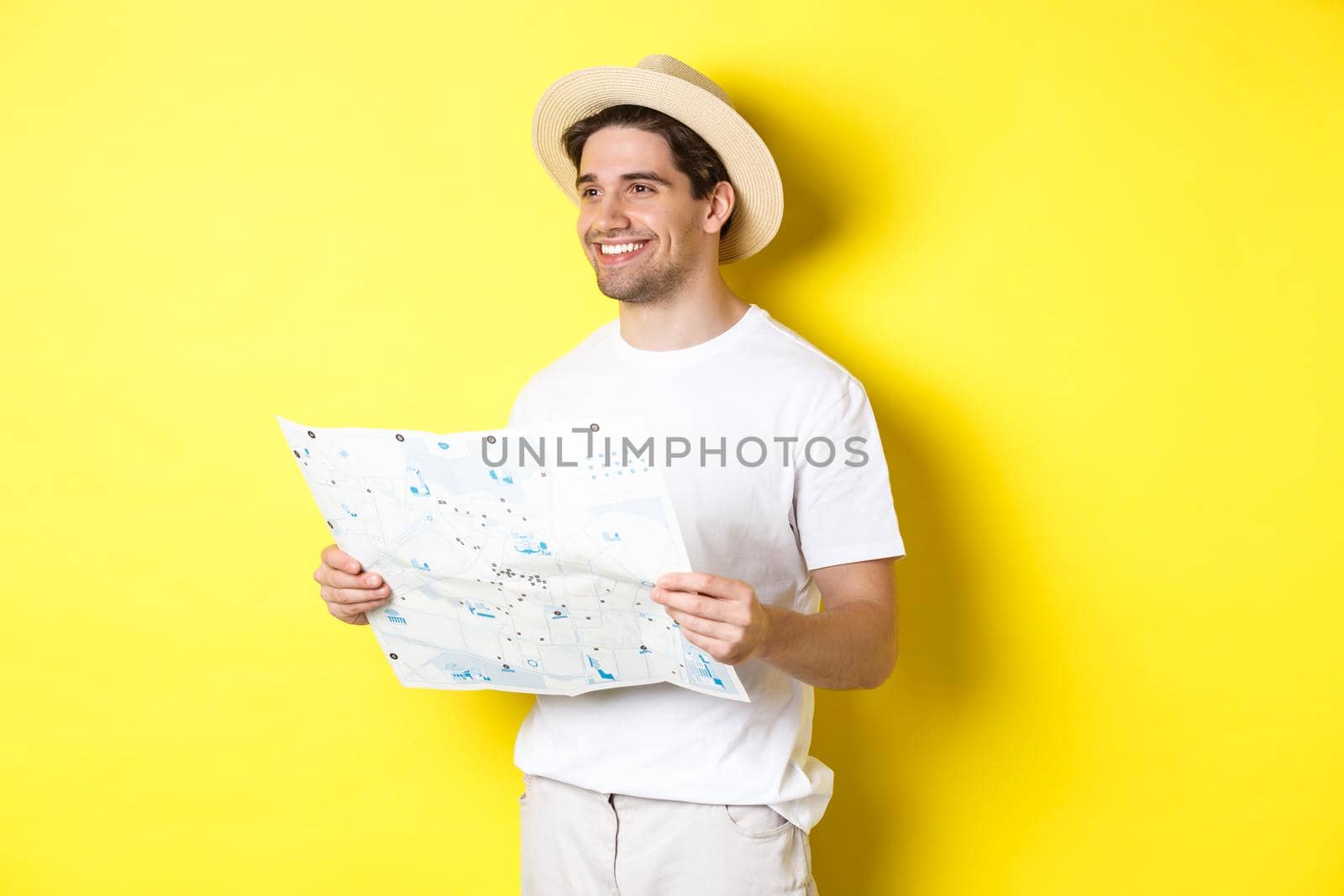 Travelling, vacation and tourism concept. Handsome guy tourist going sightseeing, holding map and smiling, standing over yellow background.