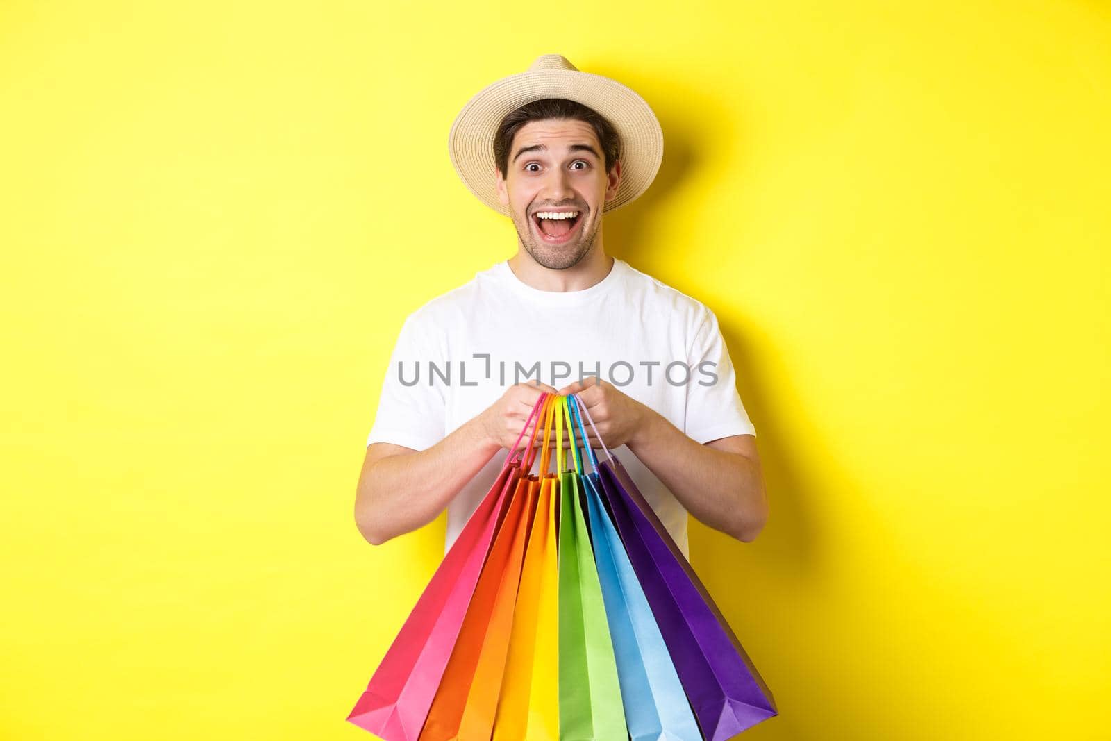 Image of happy man shopping on vacation, holding paper bags and smiling, standing against yellow background by Benzoix