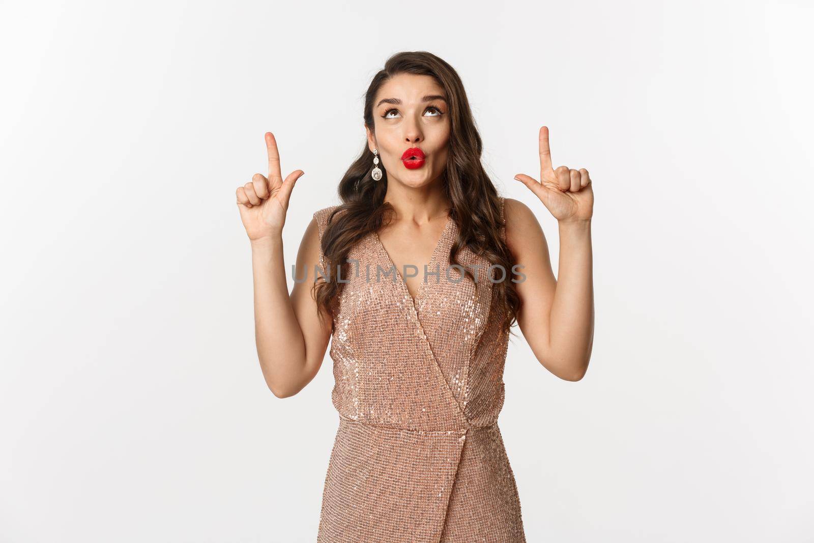 New Year, christmas and celebration concept. Beautiful curious woman in party dress, saying wow and looking at promo offer, pointing fingers up, showing advertisement.