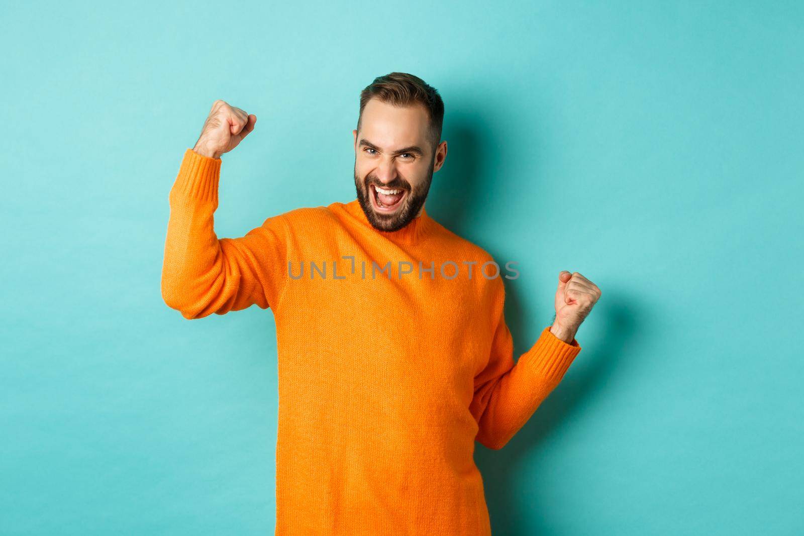 Winner. Excited man triumphing, making fist pump and saying yes, triumphing and looking satisfied, achieve goal, standing over light blue background.