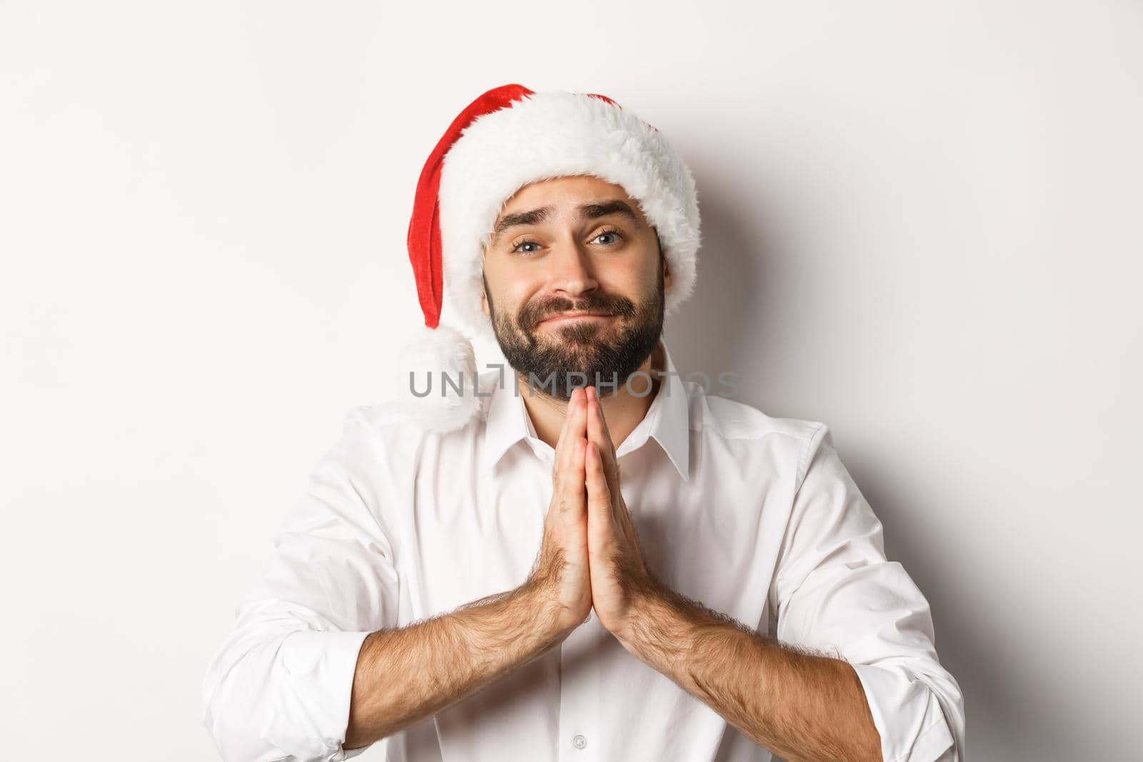 Party, winter holidays and celebration concept. Close-up of adult guy in santa hat begging for christmas gift, holding hands in plead and asking for something, white background.