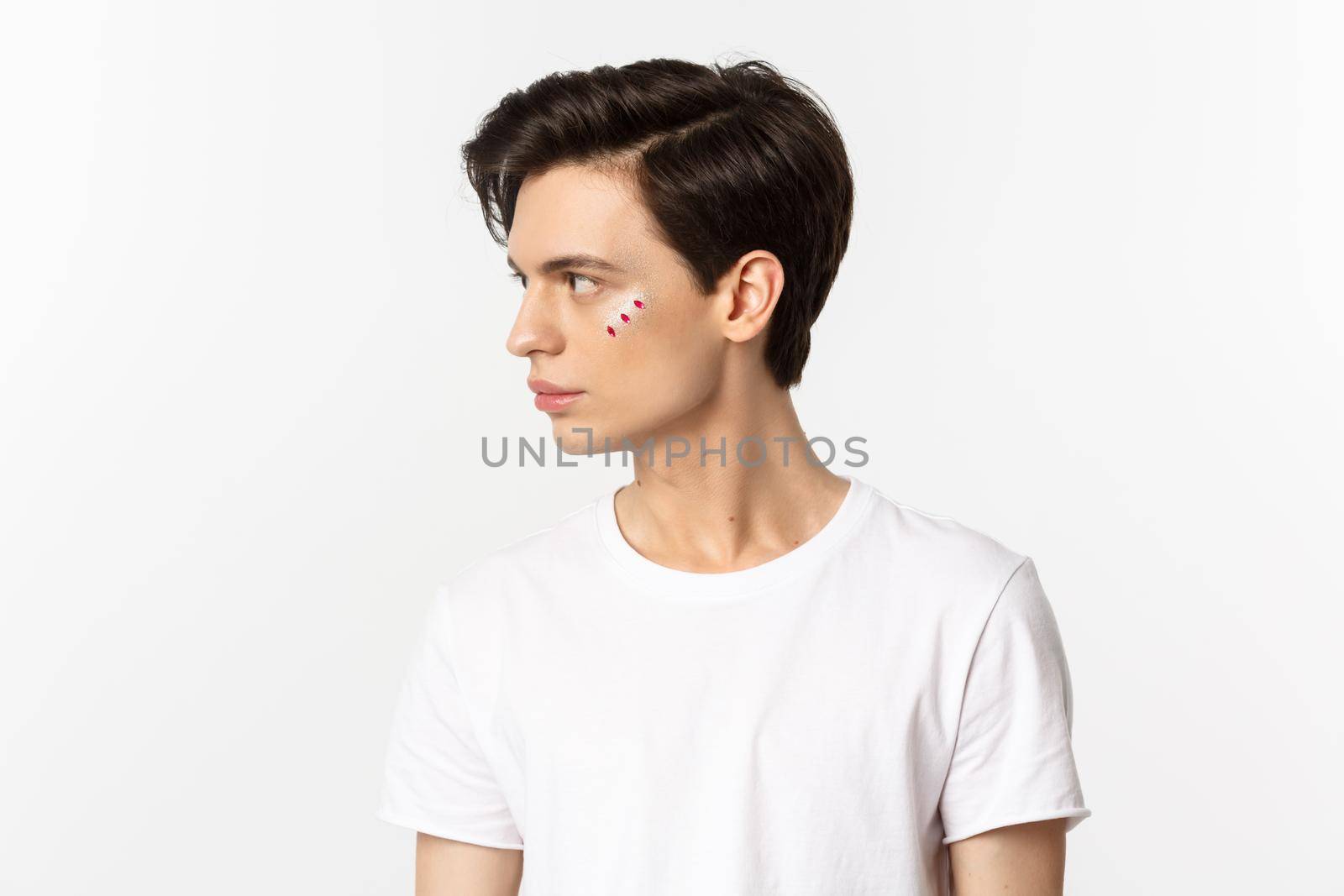 People, lgbtq community and lifestyle concept. Profile view of handsome gay man with glitter on face, looking left, standing over white background.