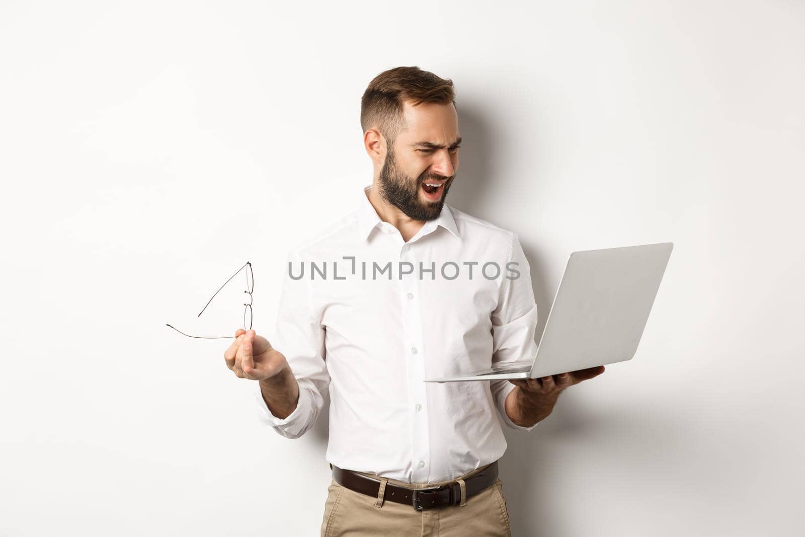 Confused manager looking at laptop, standing disappointed against white background by Benzoix