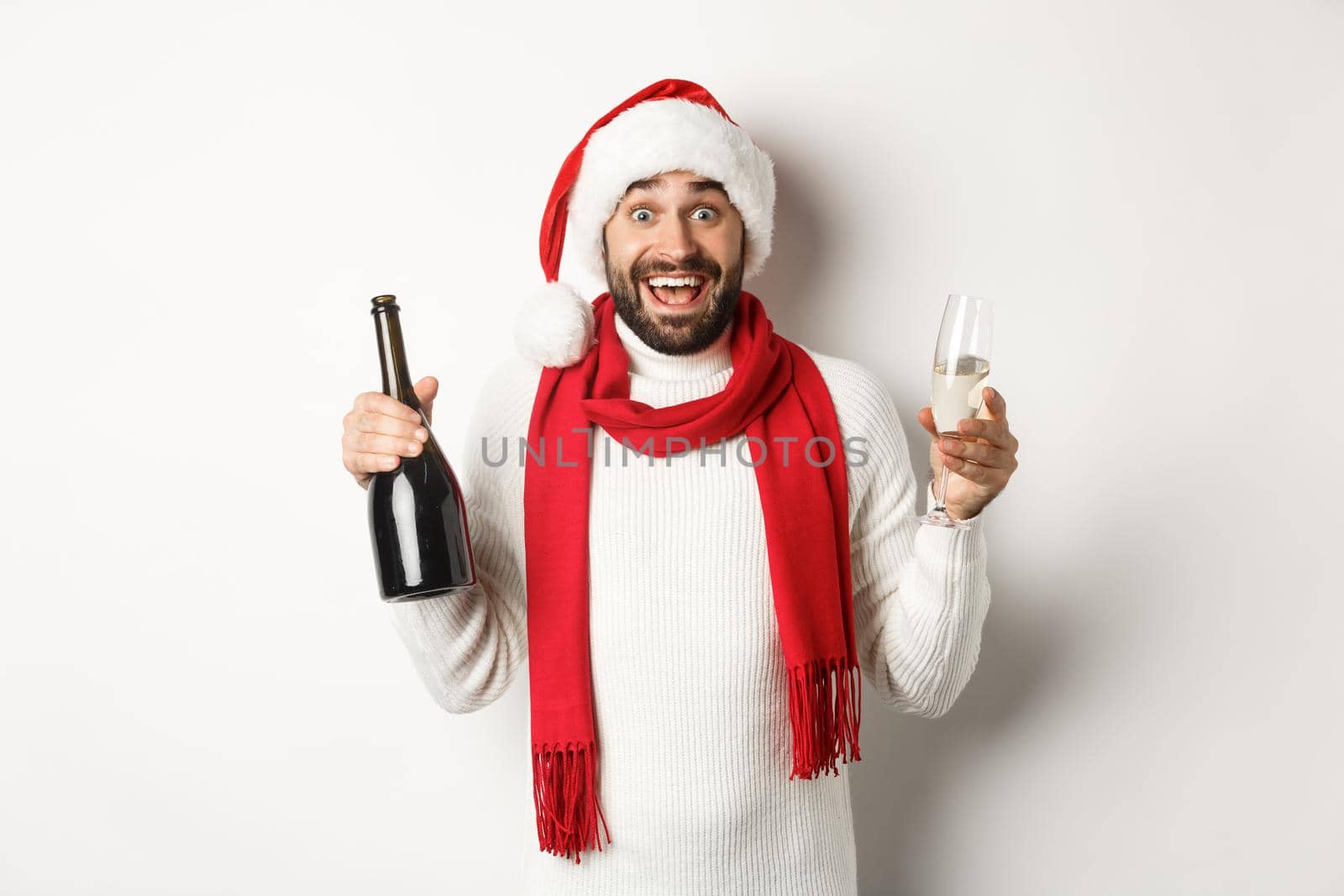 Christmas party and holidays concept. Happy bearded male model in Santa hat and red scarf, celebrating xmas, partying with glass of Champgne, white background.