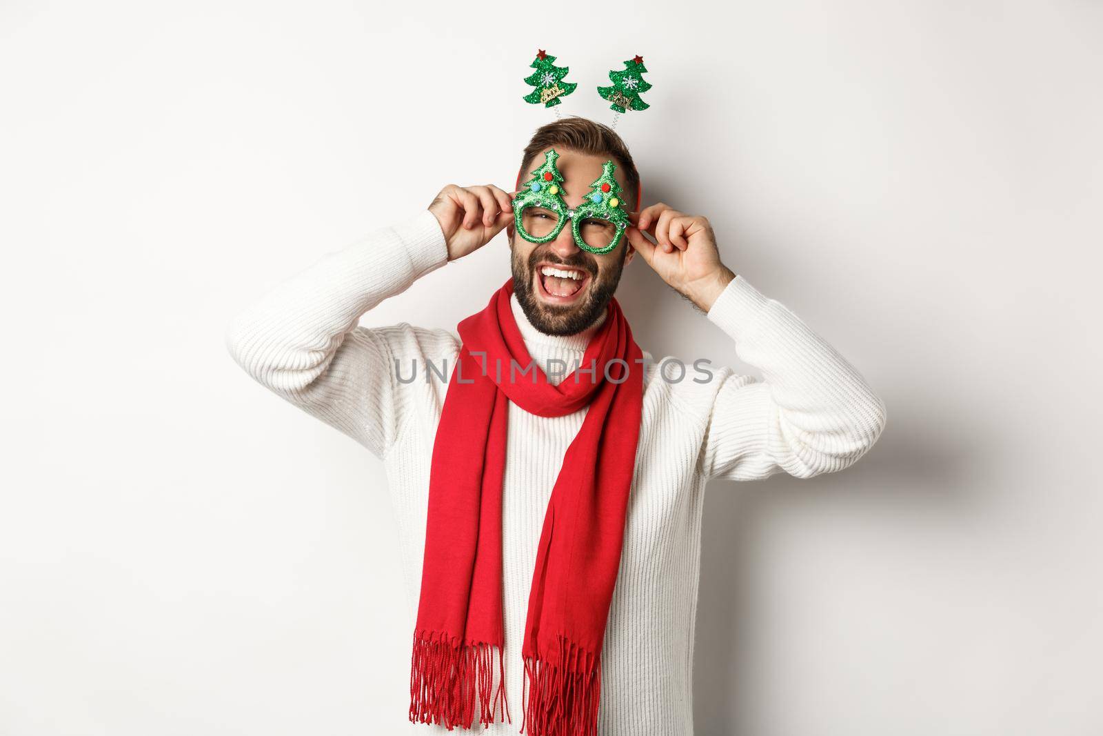 Christmas, New Year and celebration concept. Handsome guy celebrating, put on party glasses and accessory, laughing happy, standing over white background.