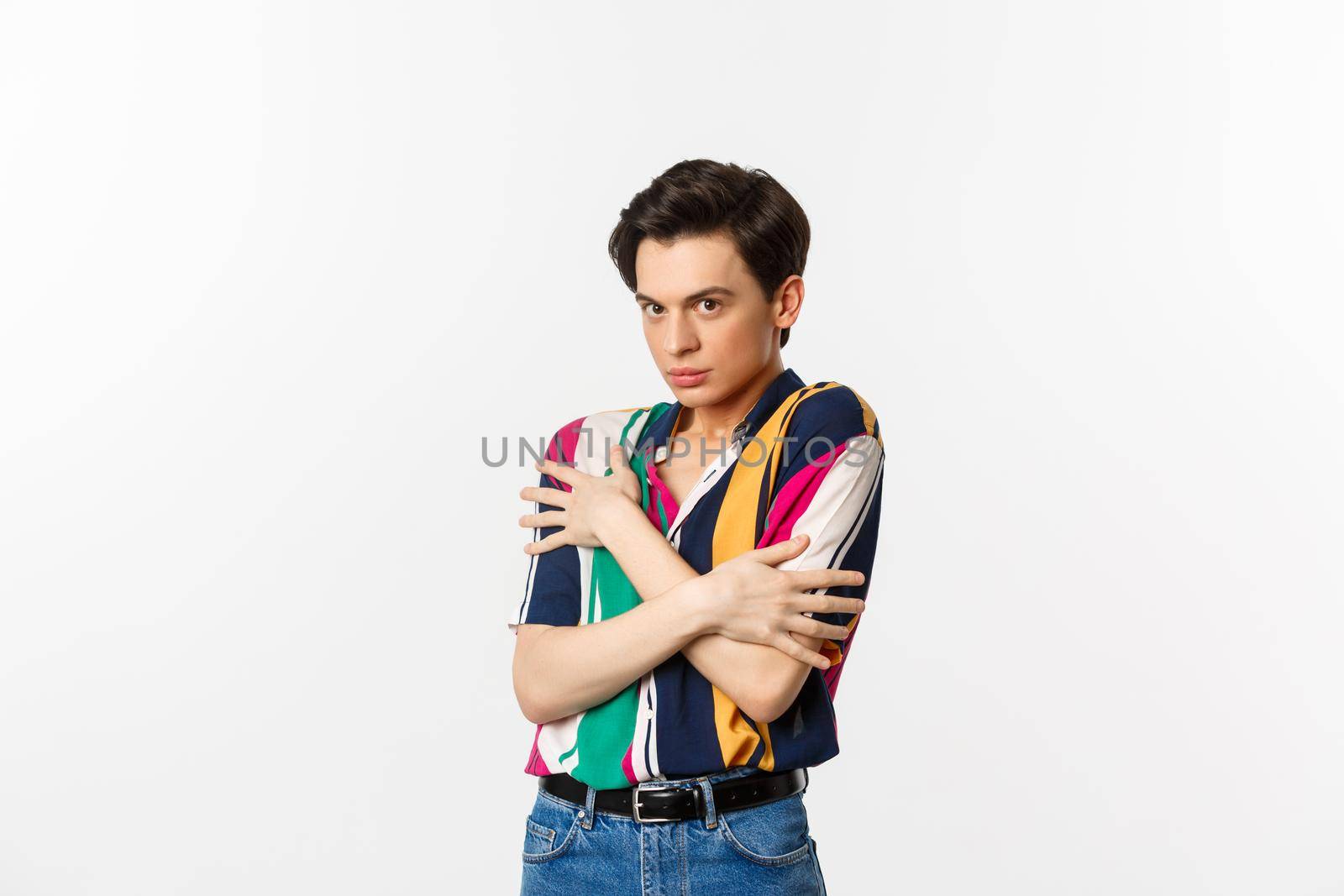 Image of timid gay man cringe and looking displeased at camera, hugging himself defensive, standing over white background by Benzoix