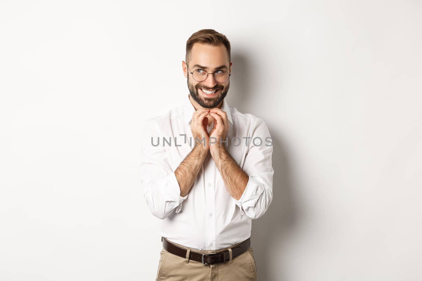 Young cunning businessman steeple fingers and smiling devious, scheming plan, standing over white background.