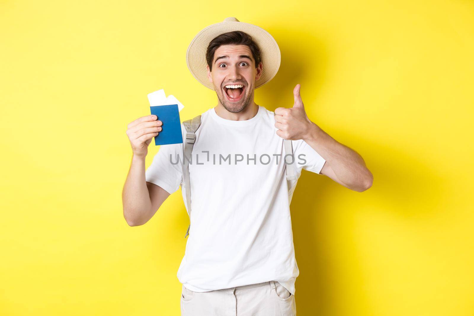 Tourism and vacation. Satisfied male tourist showing passport with tickets and thumb up, recommending travel company, standing over yellow background by Benzoix