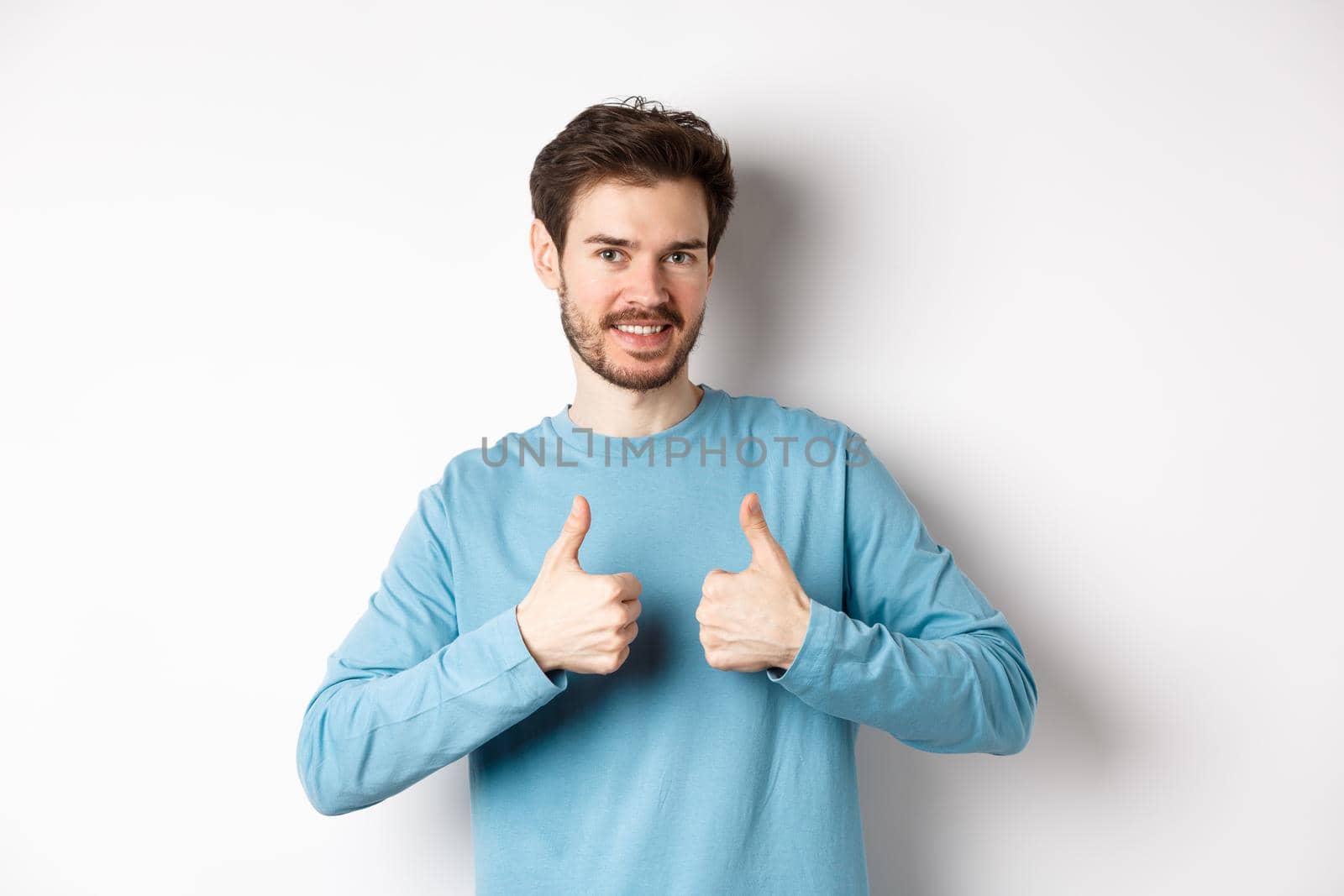 Good choice. Attractive caucasian man with beard showing thumbs up and smiling, like and approve good product, recommending something, standing on white background by Benzoix